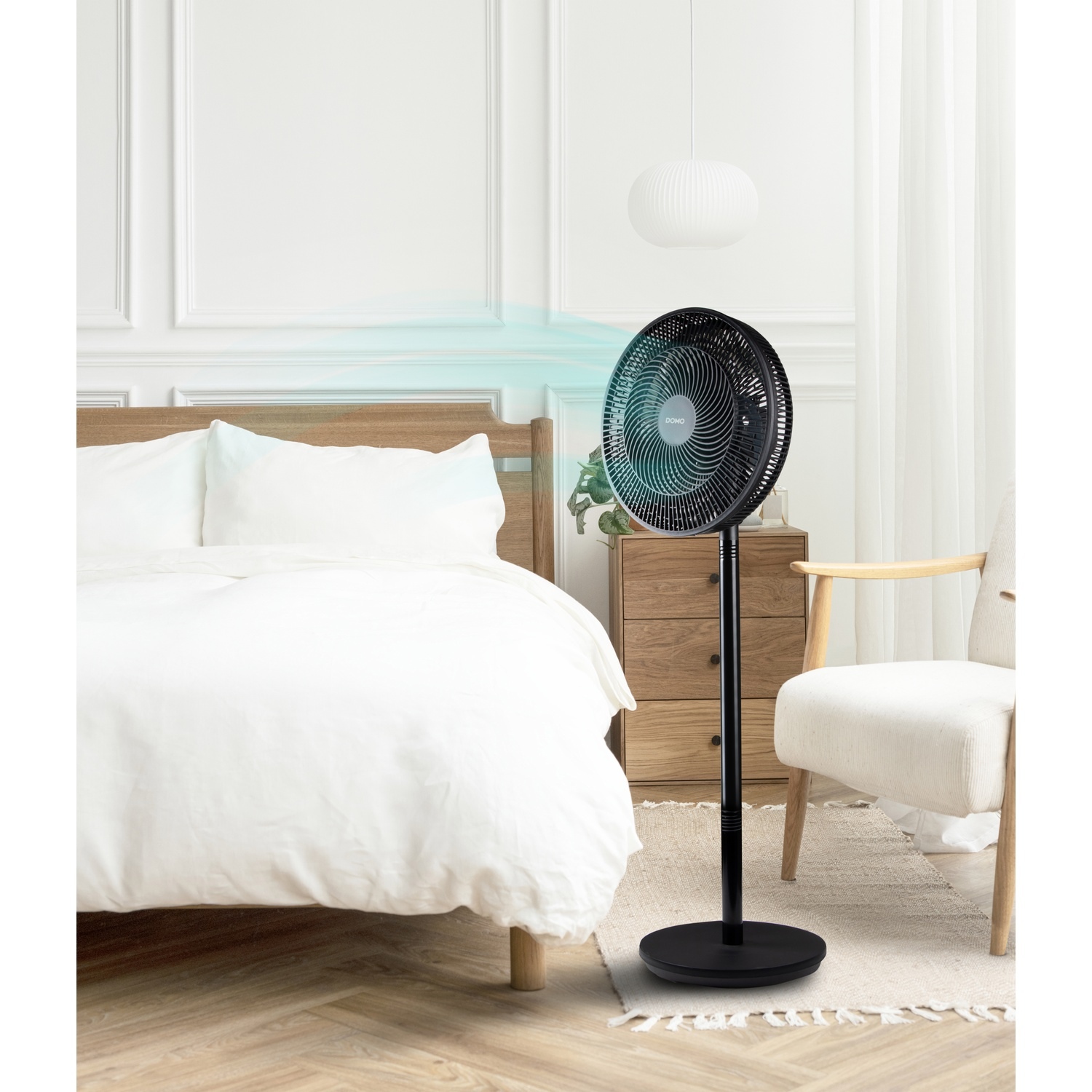 A black standing fan is placed next to a bed in a bedroom.