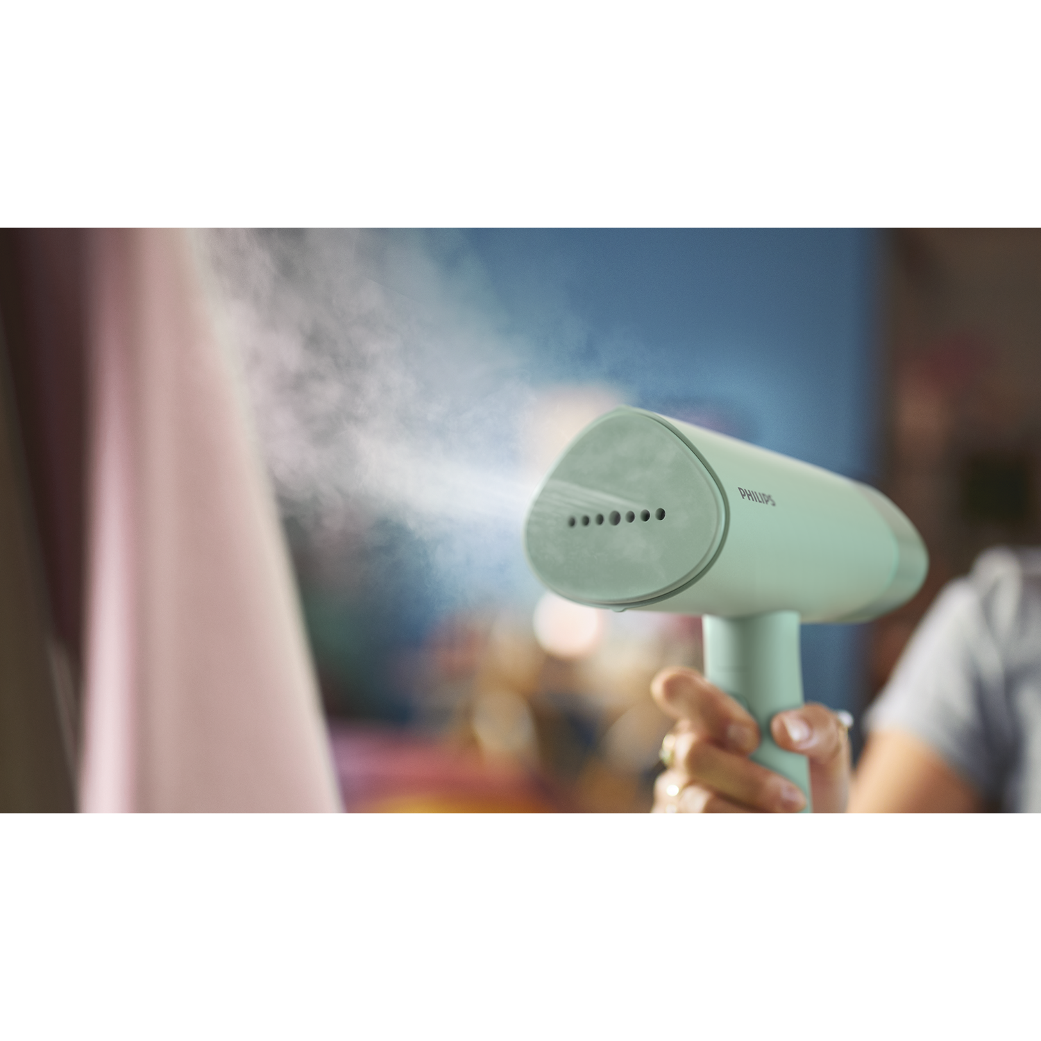Hand houdt een turkooizen Philips kledingstomer vast die stoom op een roze kledingstuk sproeit.
