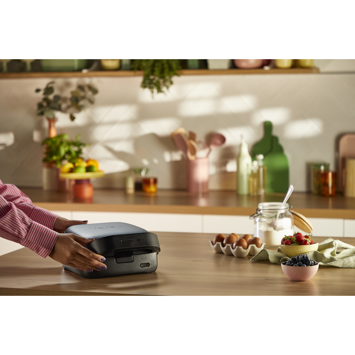 Person closing a dark kitchen appliance on a wooden table with ingredients.