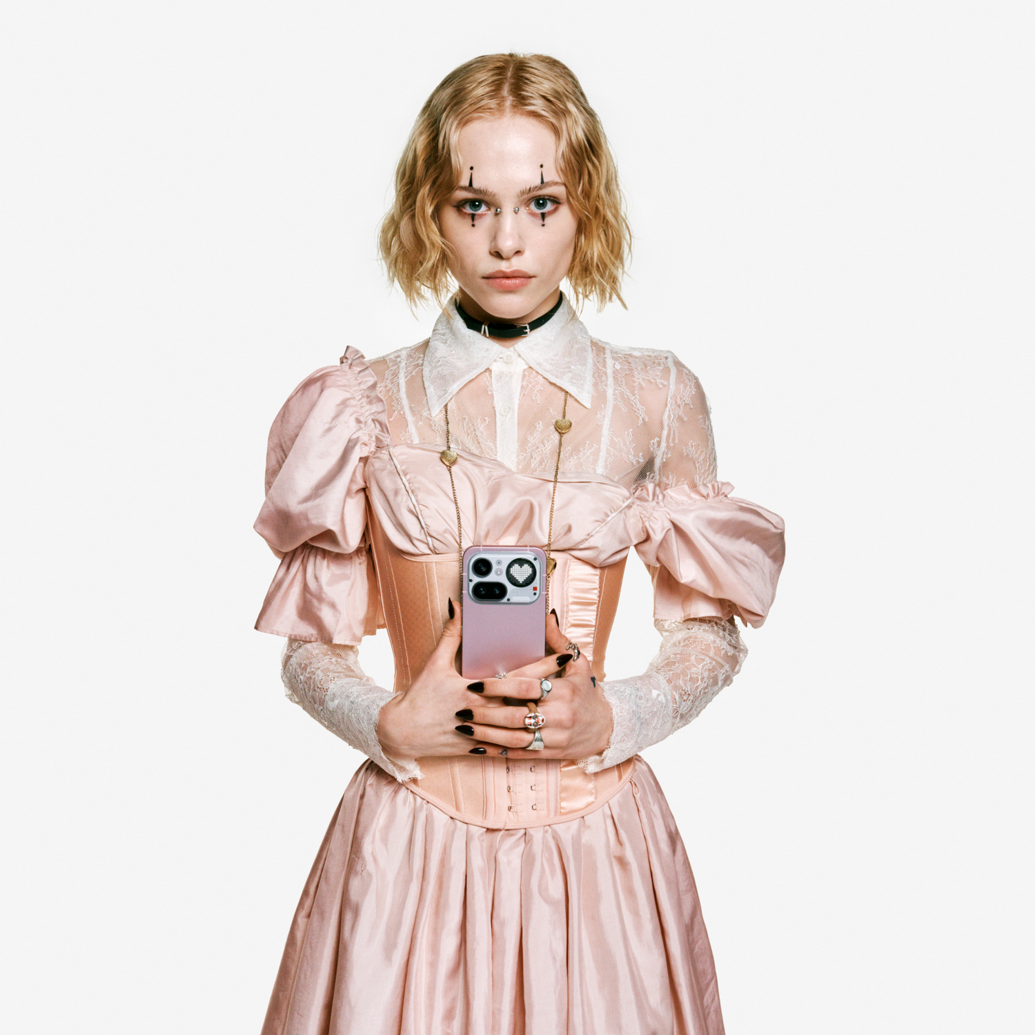Mujer con vestido rosa y encaje, sosteniendo un teléfono rosa. Fondo blanco.