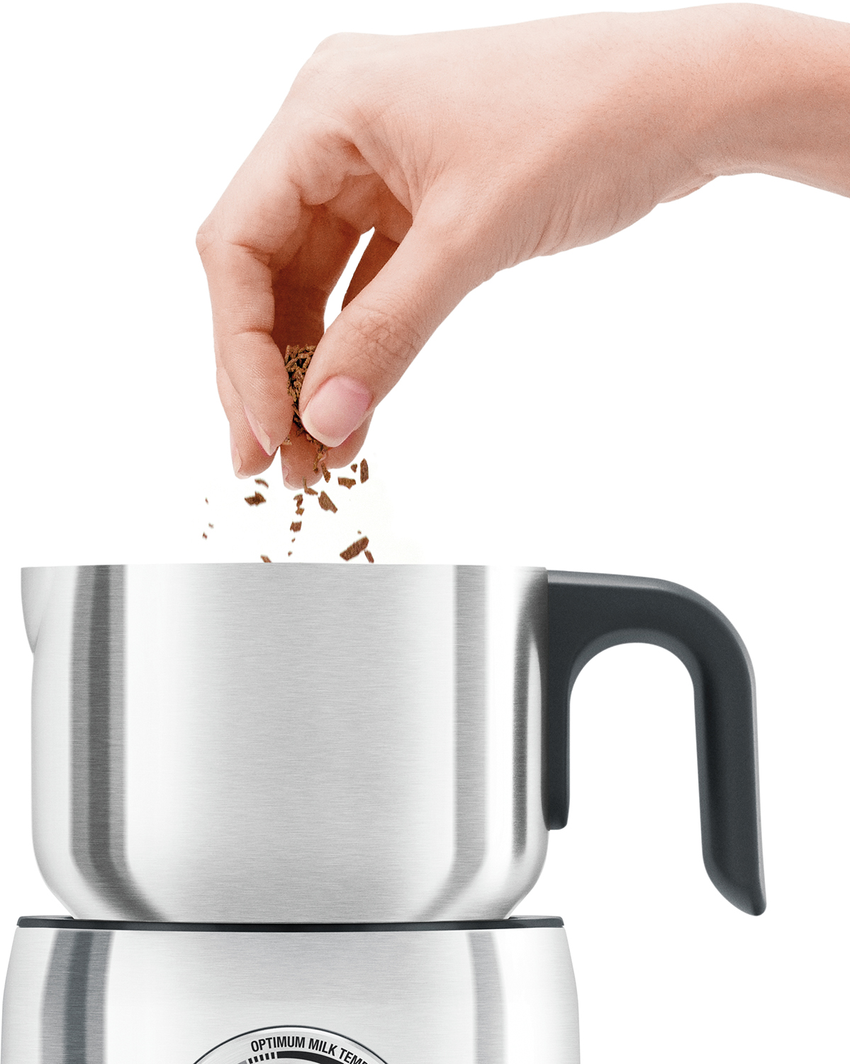 Una mano esparce posos de café en un espumador de leche plateado.