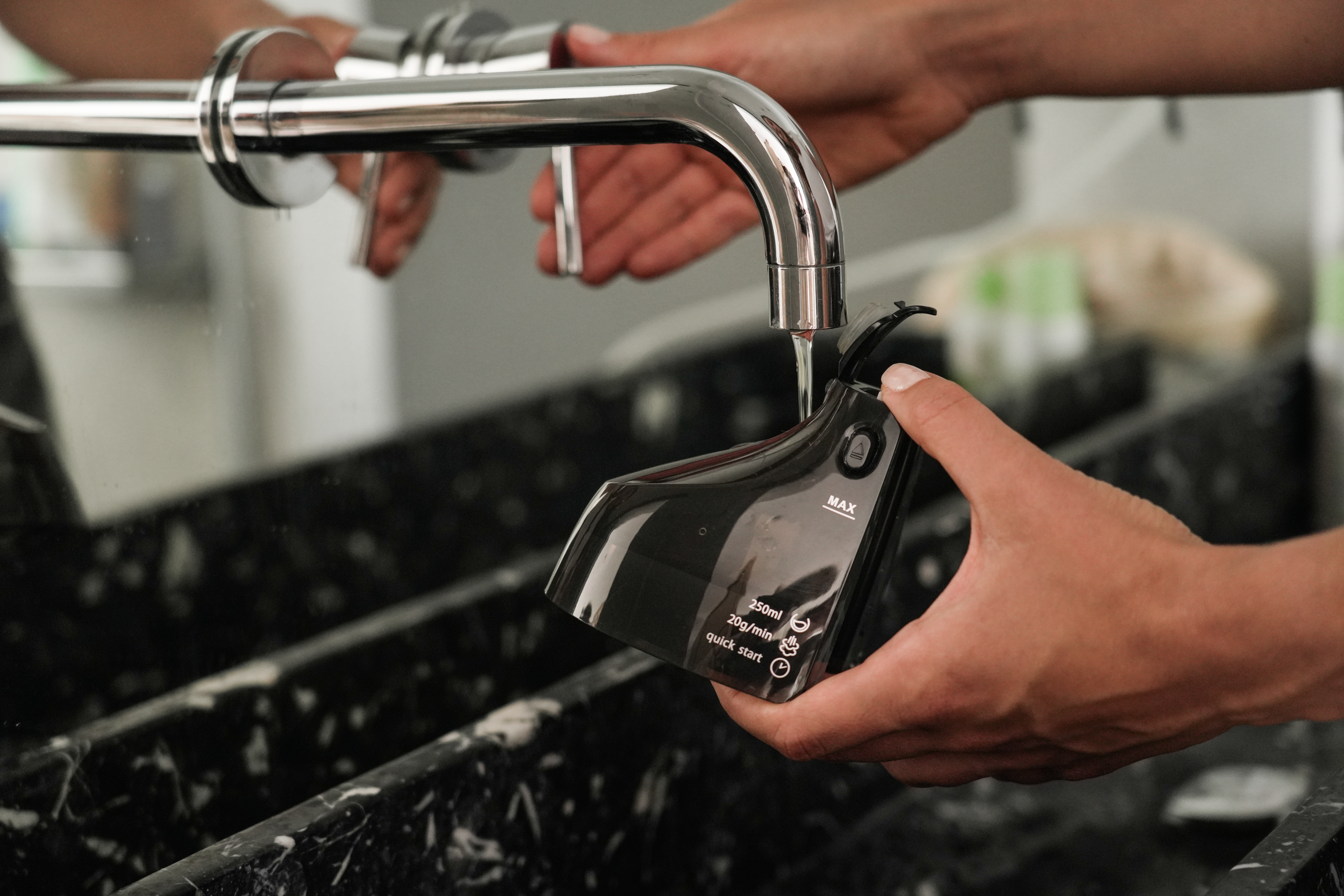 El agua fluye hacia un dispositivo negro sostenido por manos bajo un grifo.
