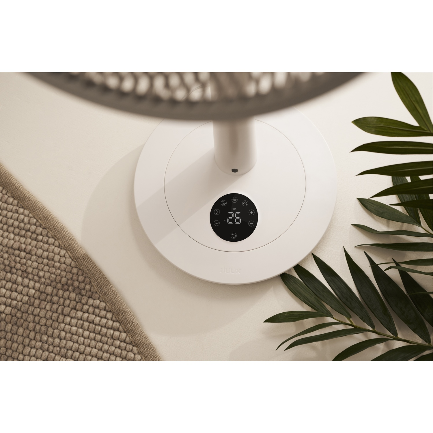 Base blanche de ventilateur avec écran numérique affichant 26°C. Feuilles vertes à côté.
