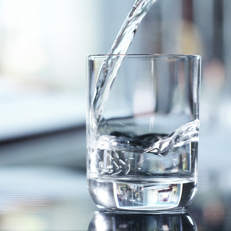 L'acqua viene versata in un bicchiere trasparente su una superficie scura.