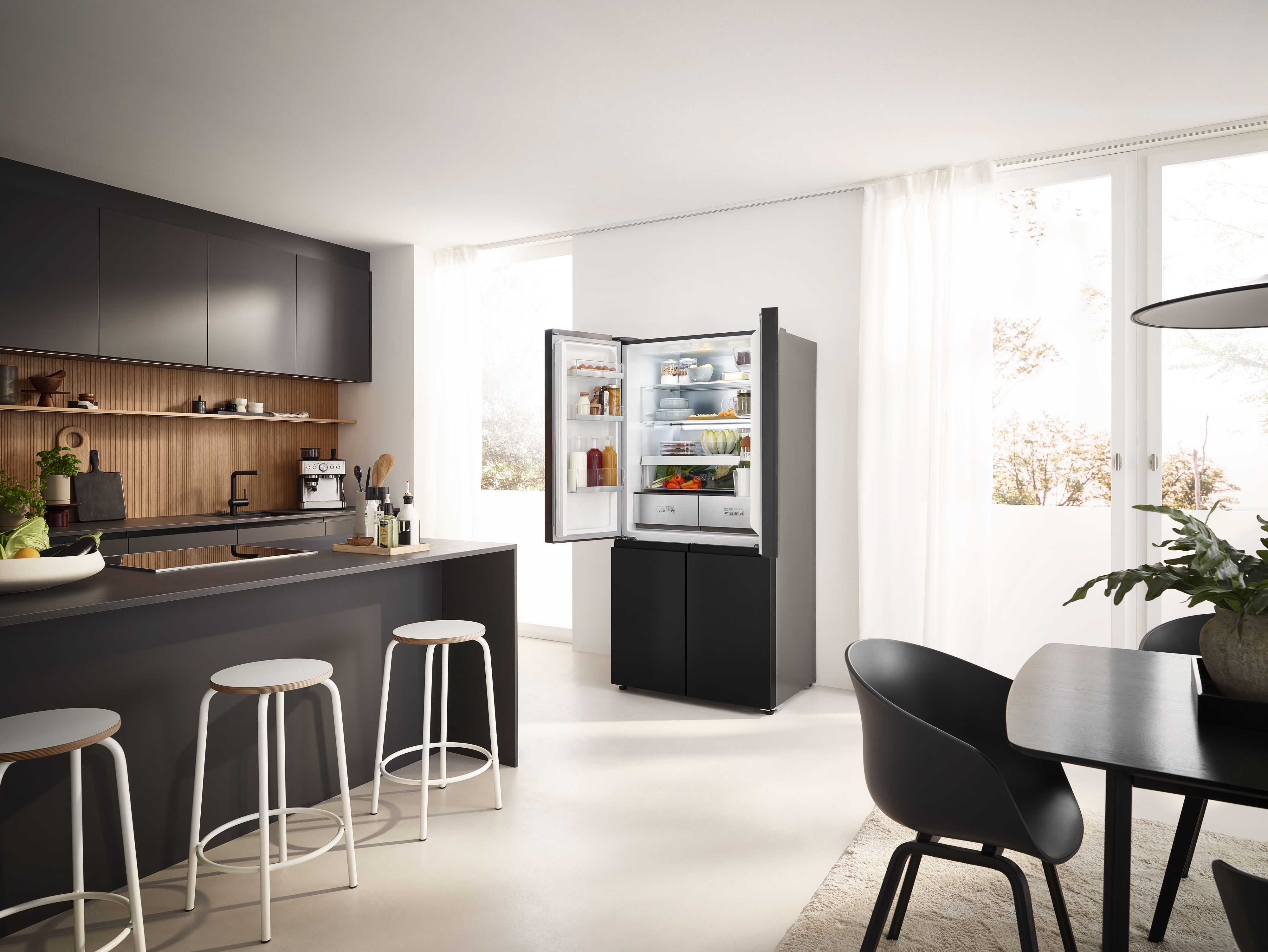Cocina moderna con refrigerador negro abierto, barra y mesa de comedor.