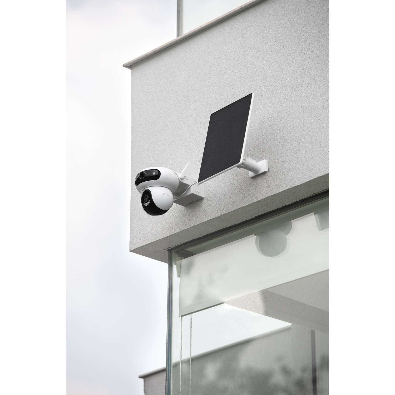 A white security camera with a solar panel mounted on a building wall.