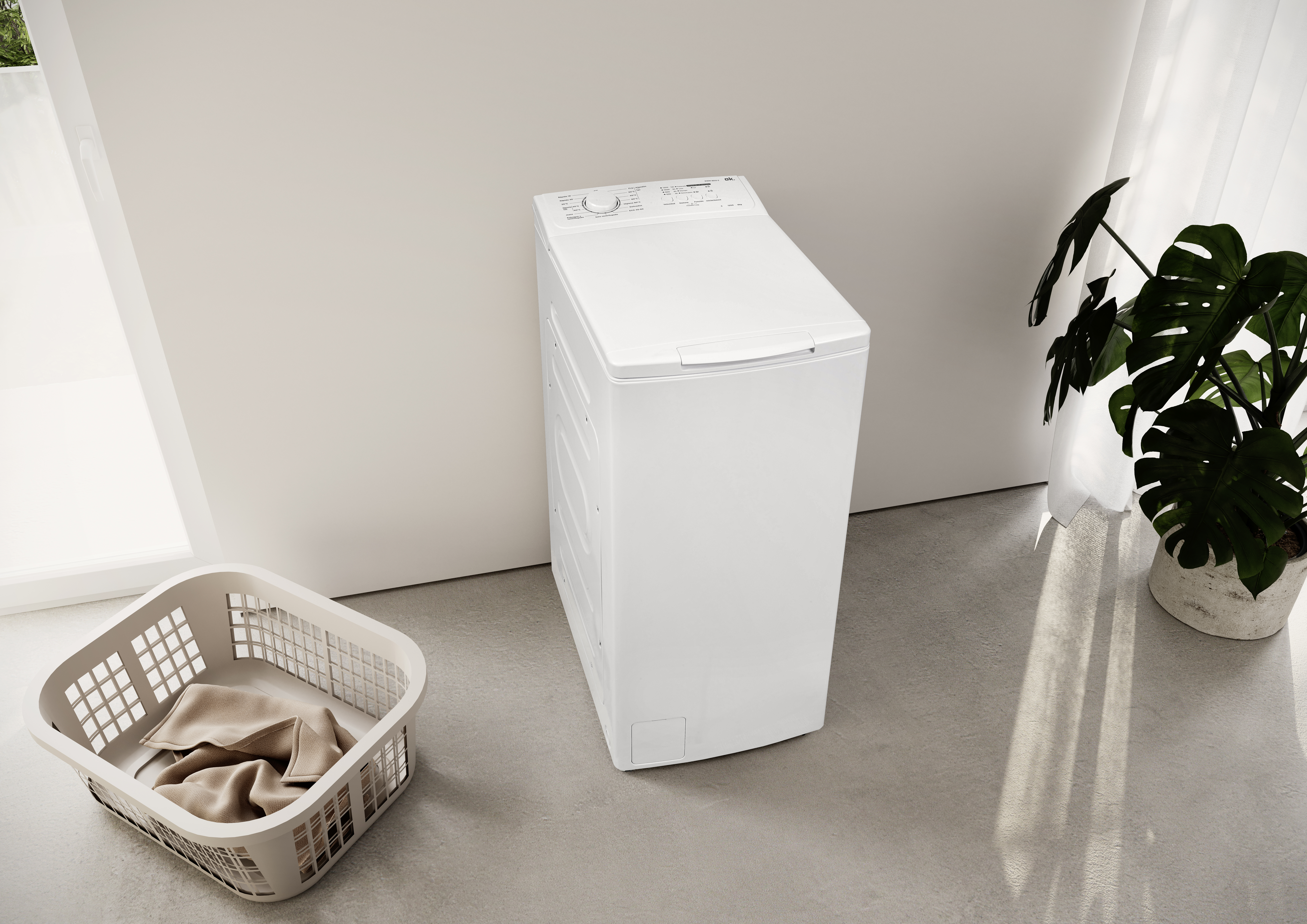 Una lavadora de carga superior blanca junto a una cesta de ropa con ropa.