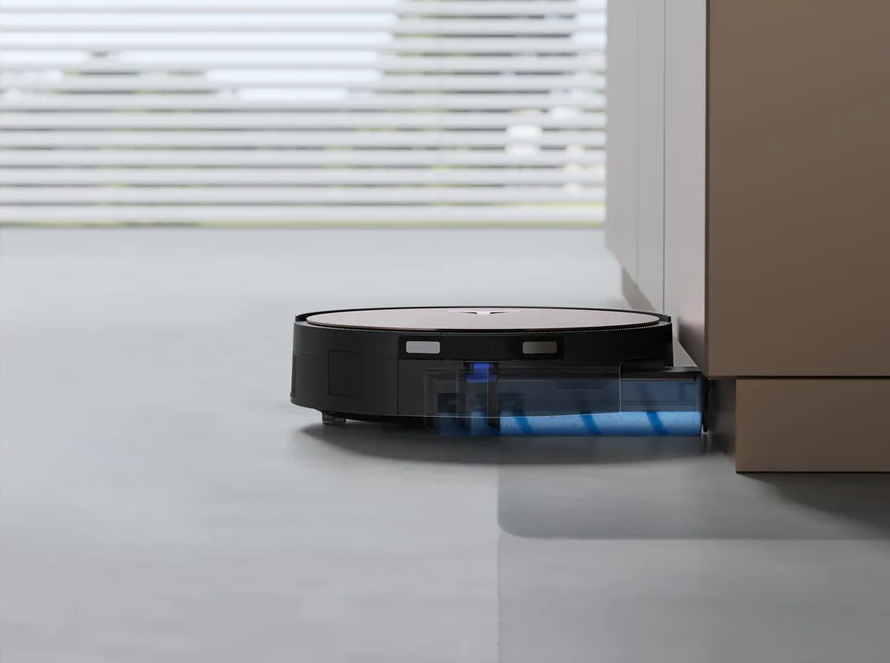 Un robot aspirapolvere nero con serbatoio dell'acqua trasparente pulisce un pavimento grigio vicino a un mobile.