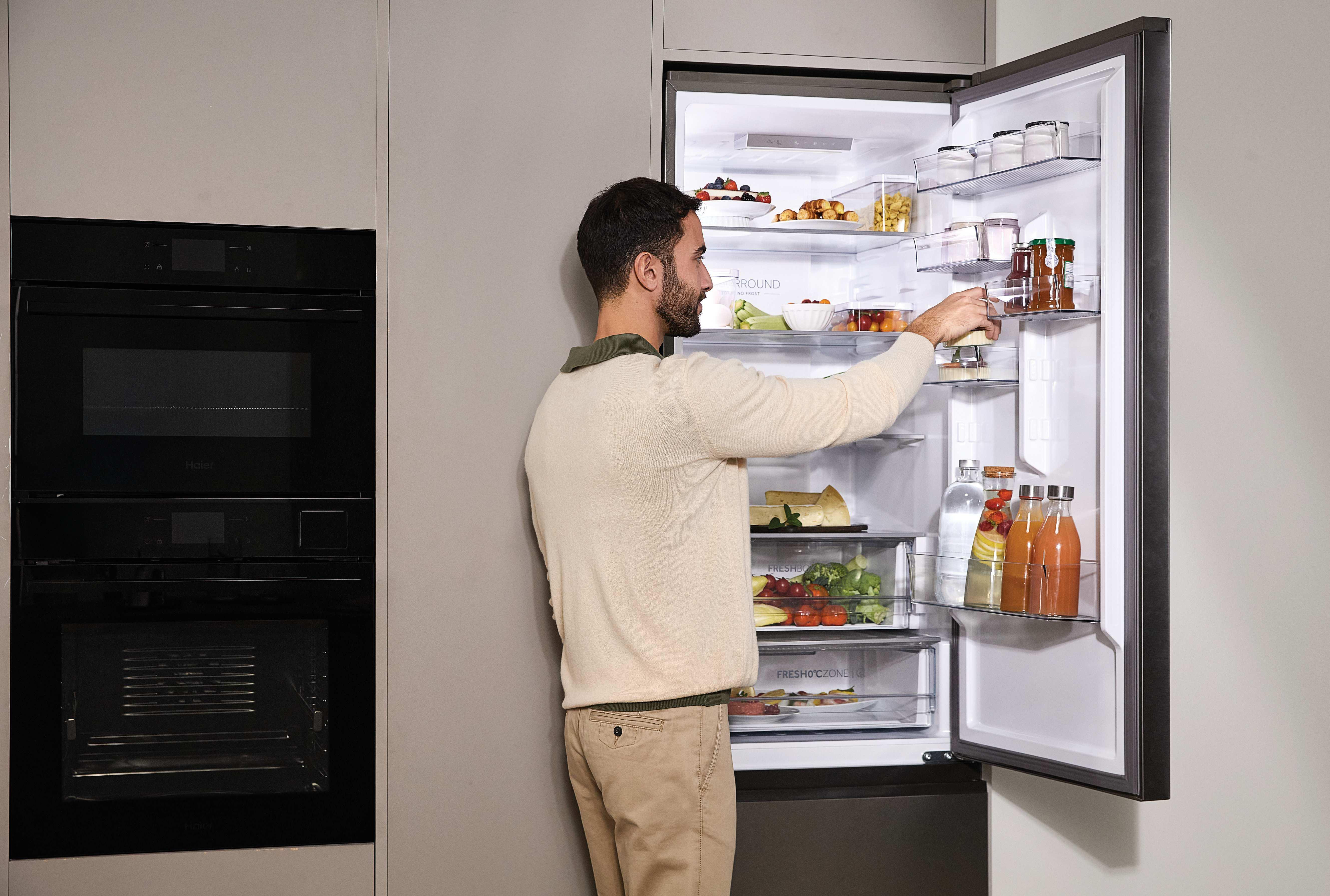 Ein Mann greift in einen geöffneten Kühlschrank, der mit Lebensmitteln gefüllt ist.