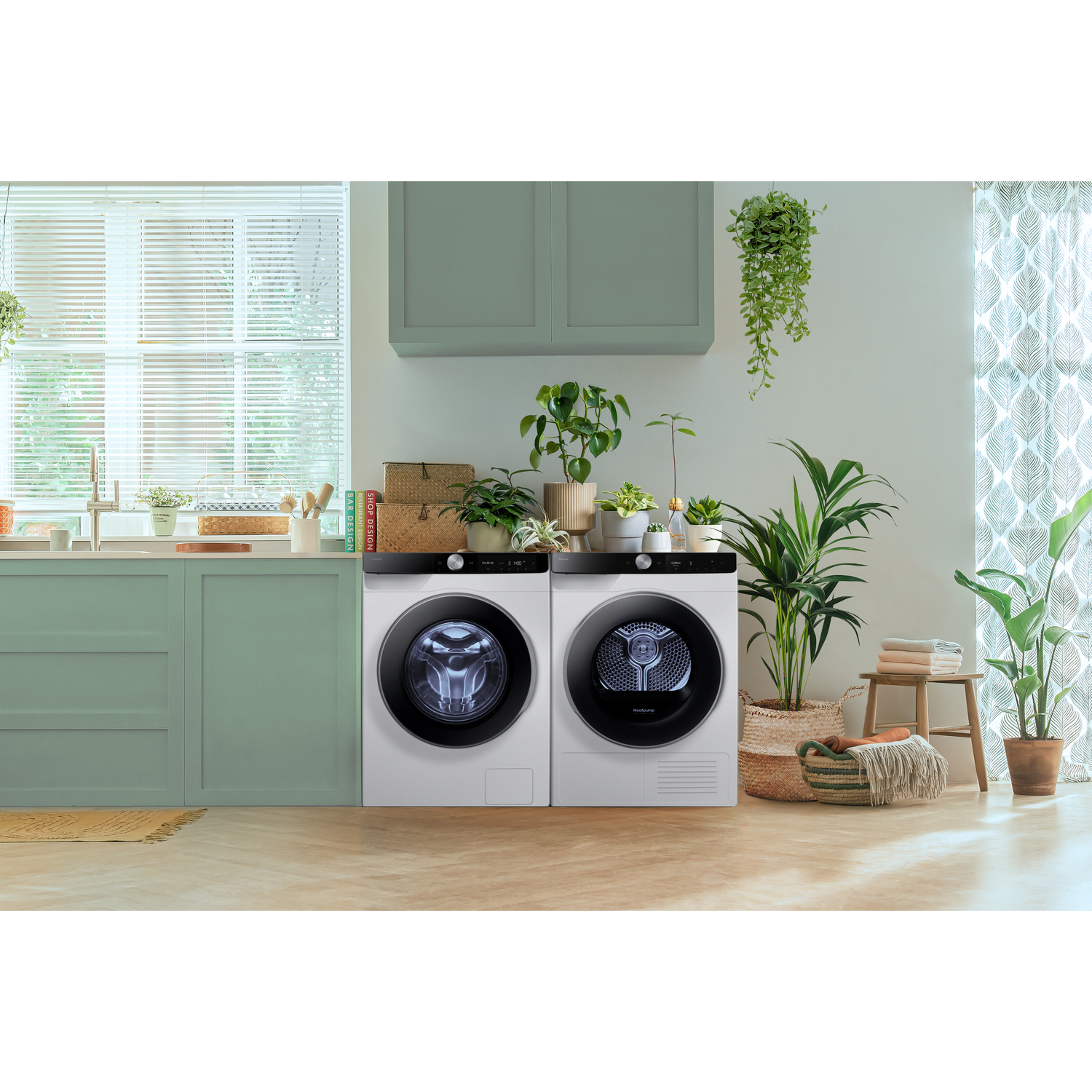 A white washer and dryer are side-by-side in a bright room with plants.
