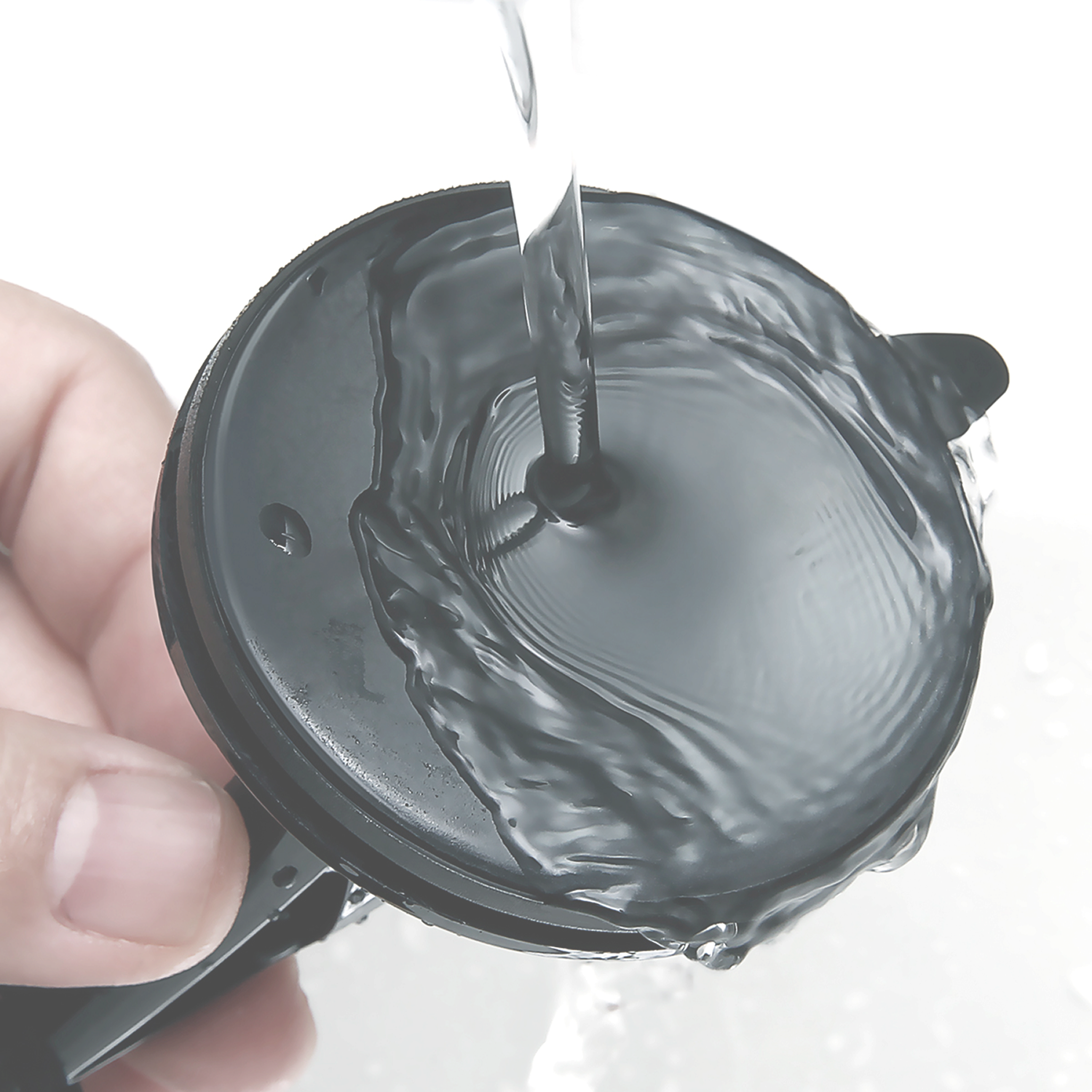 El agua fluye hacia un recipiente negro sostenido por una mano.