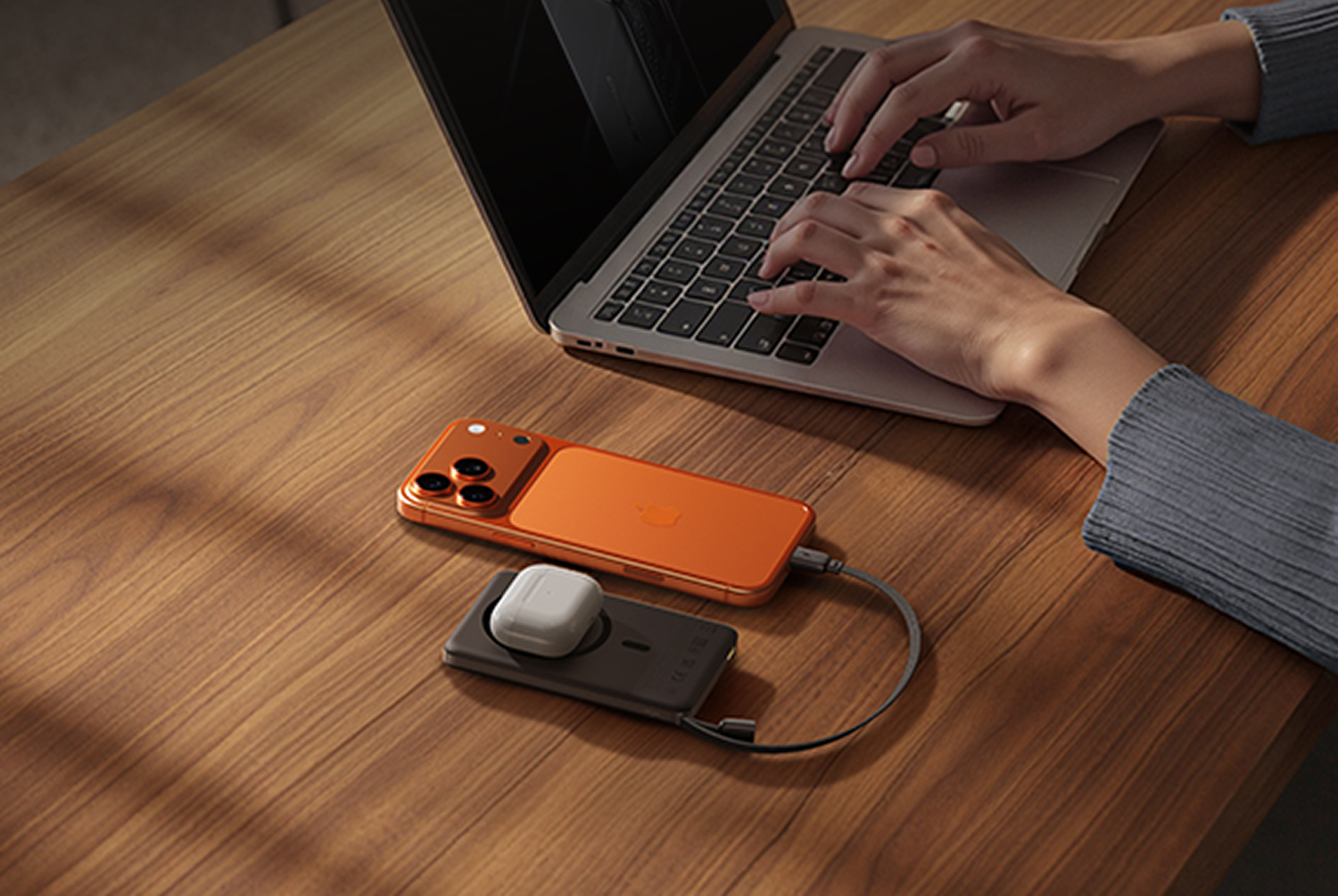 iPhone naranja con accesorios de carga y portátil en escritorio madera.