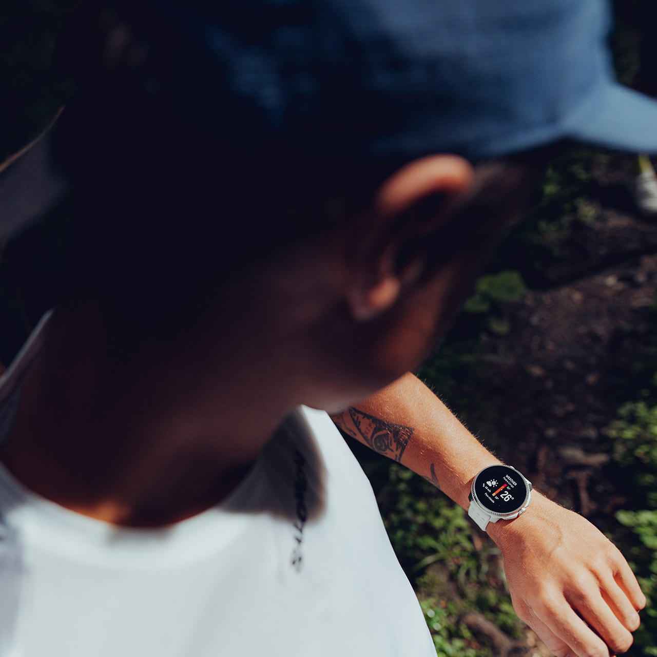 Eine Person in weißem Hemd und blauer Kappe prüft eine weiße Smartwatch am Handgelenk.