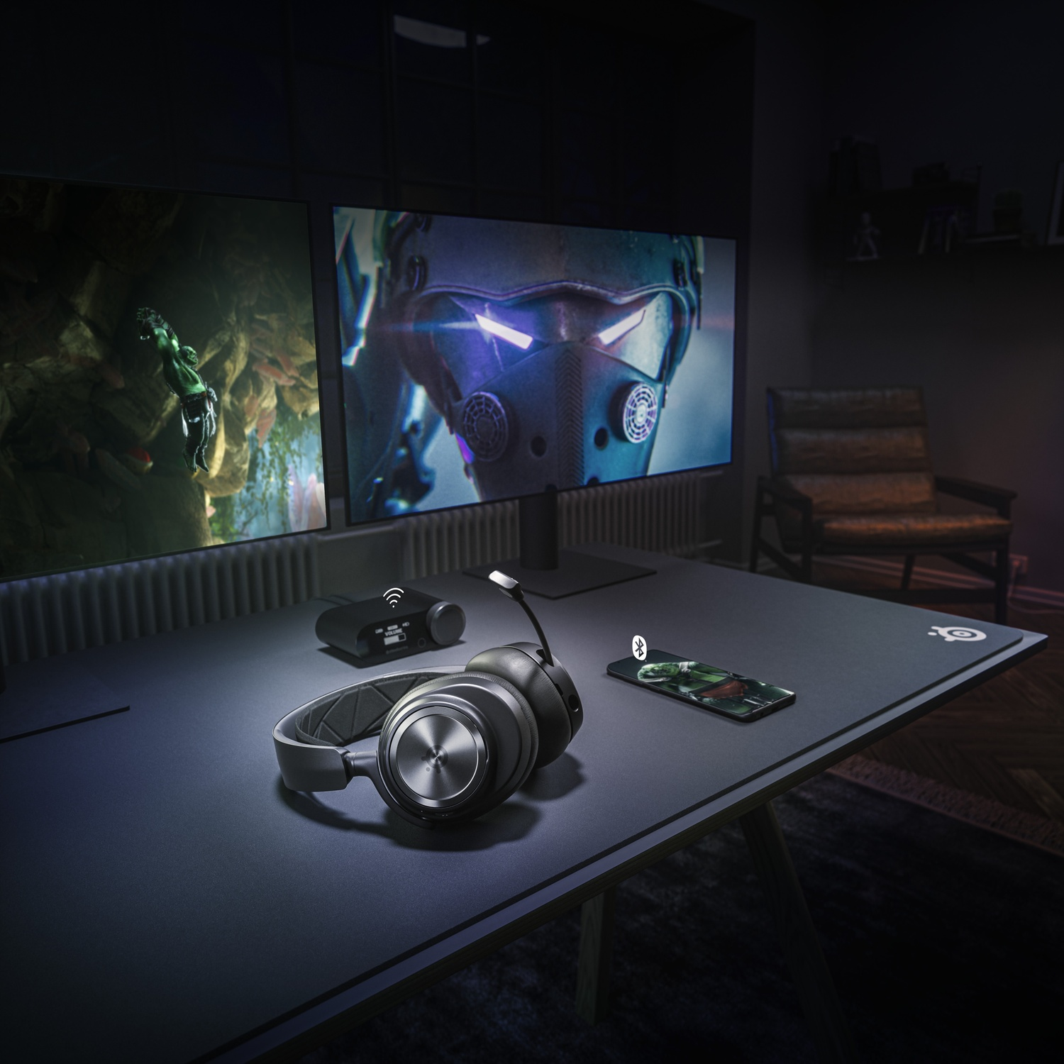 Configurazione da gioco con cuffie, smartphone e due monitor che mostrano scene di gioco.