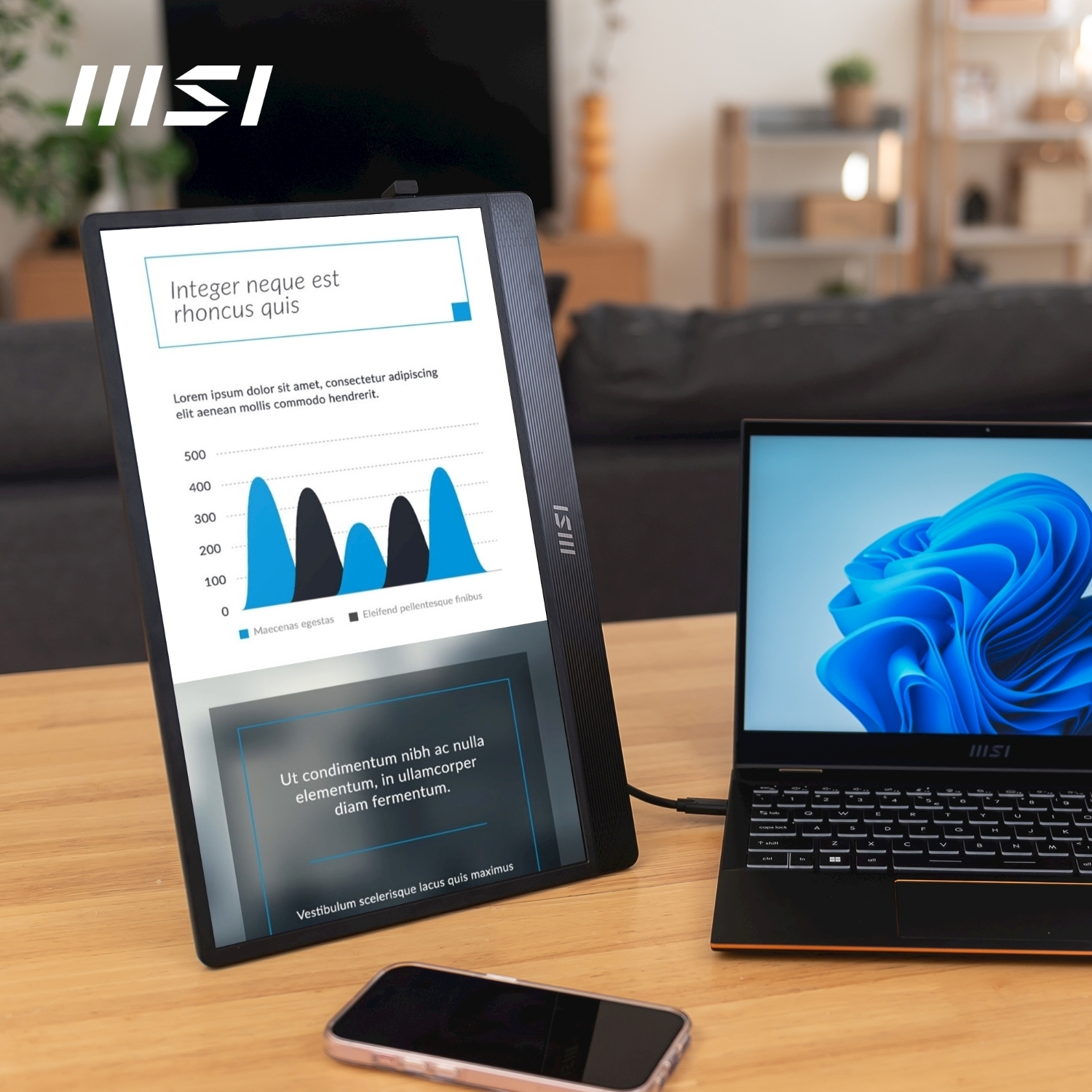 Un laptop con sfondo blu, display MSI con grafici e smartphone su tavolo in legno.