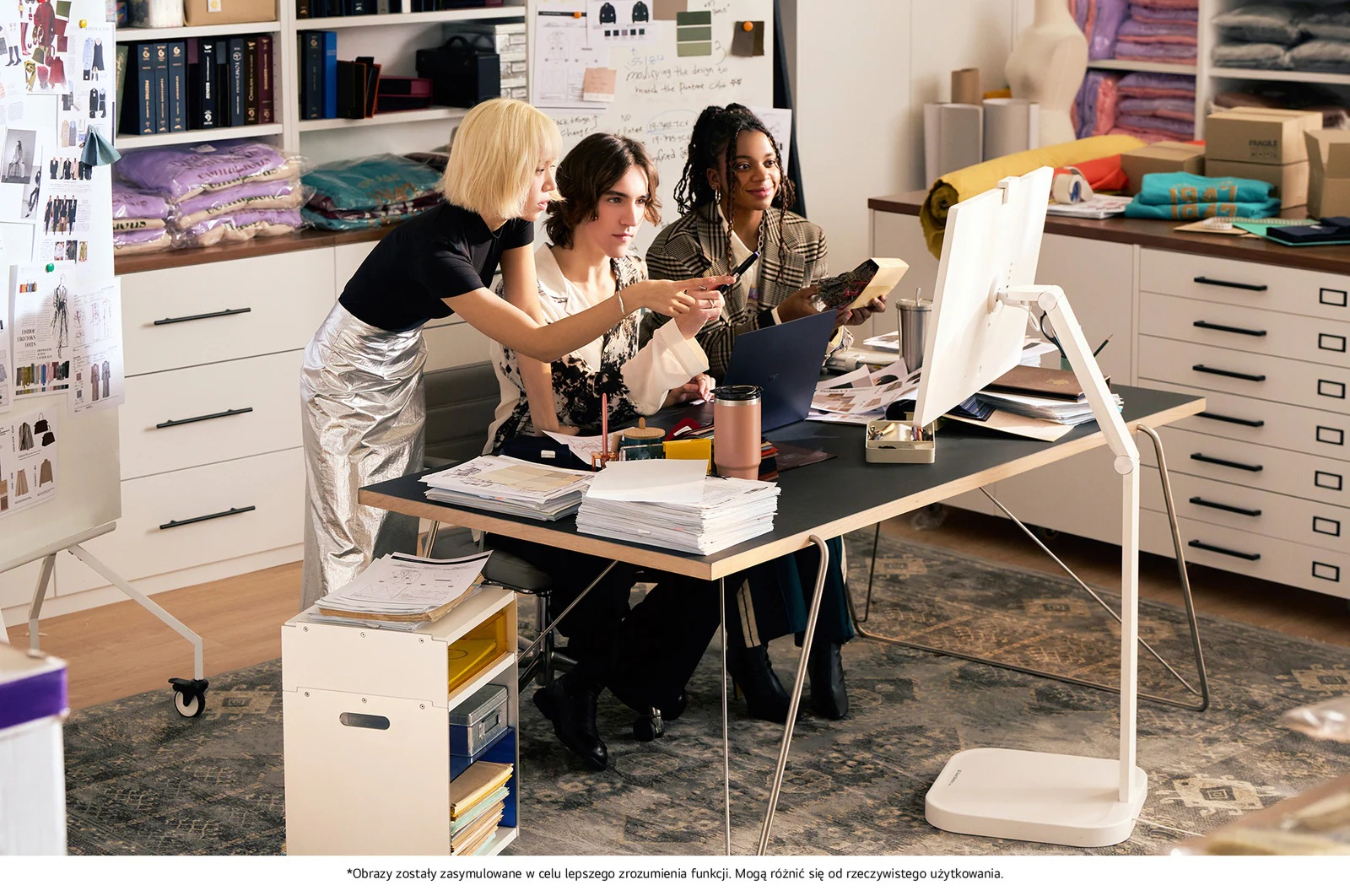 Trzy kobiety pracują przy biurku z komputerem i tkaninami w biurze.