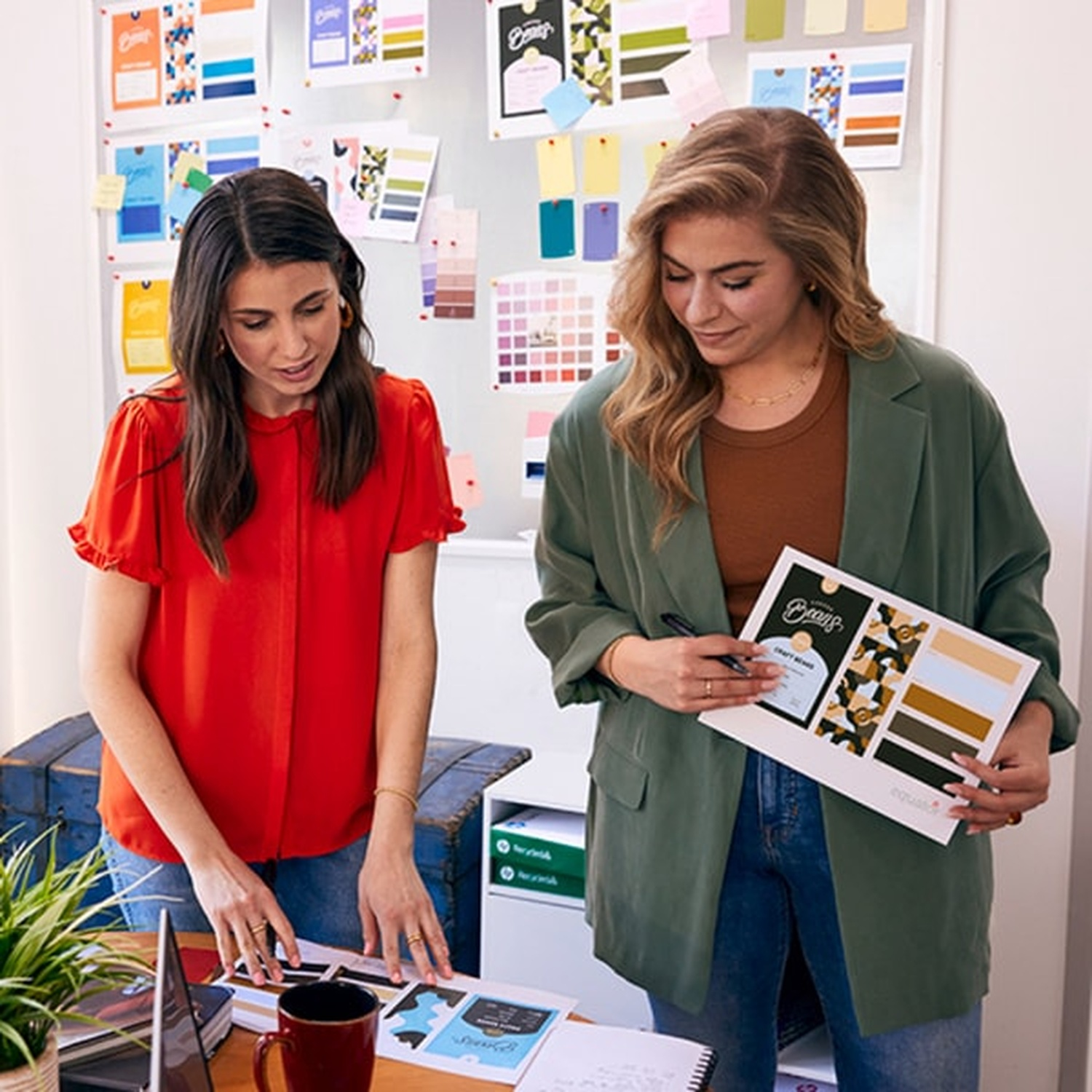Two women work on a design project, with mood boards and color swatches.