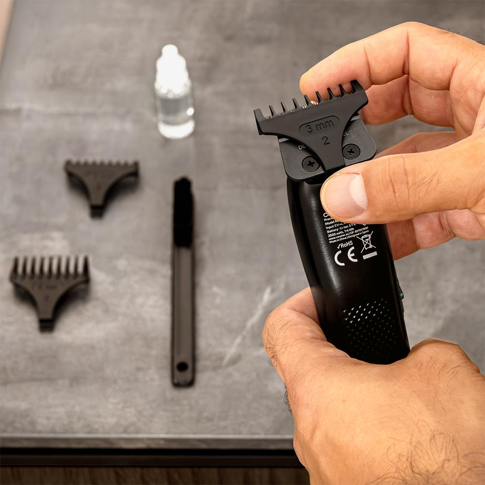 Una mano sostiene un recortador negro con accesorio de 3mm. Hay accesorios cerca.