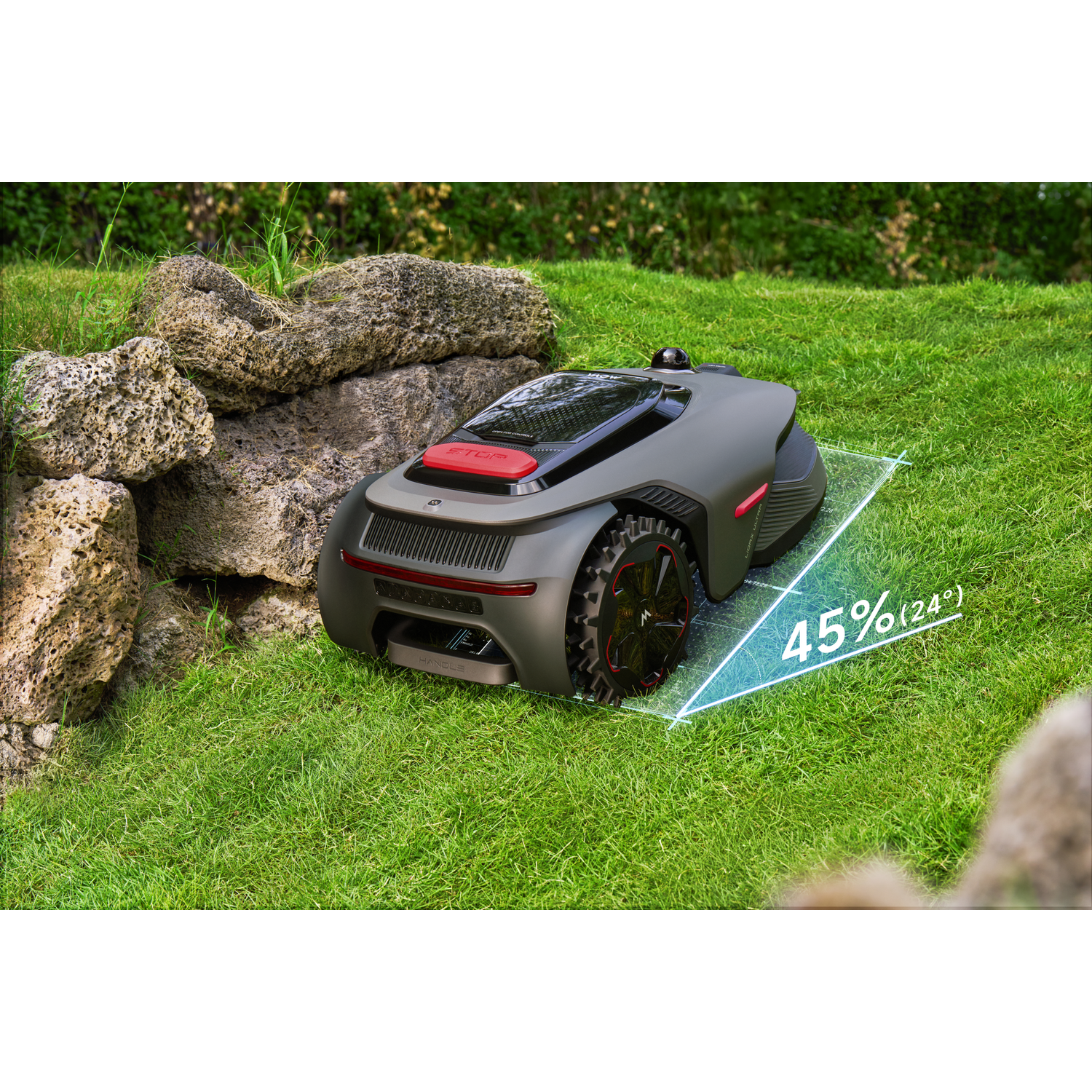 A grey lawn mower robot with red accents sits on grass next to rocks.