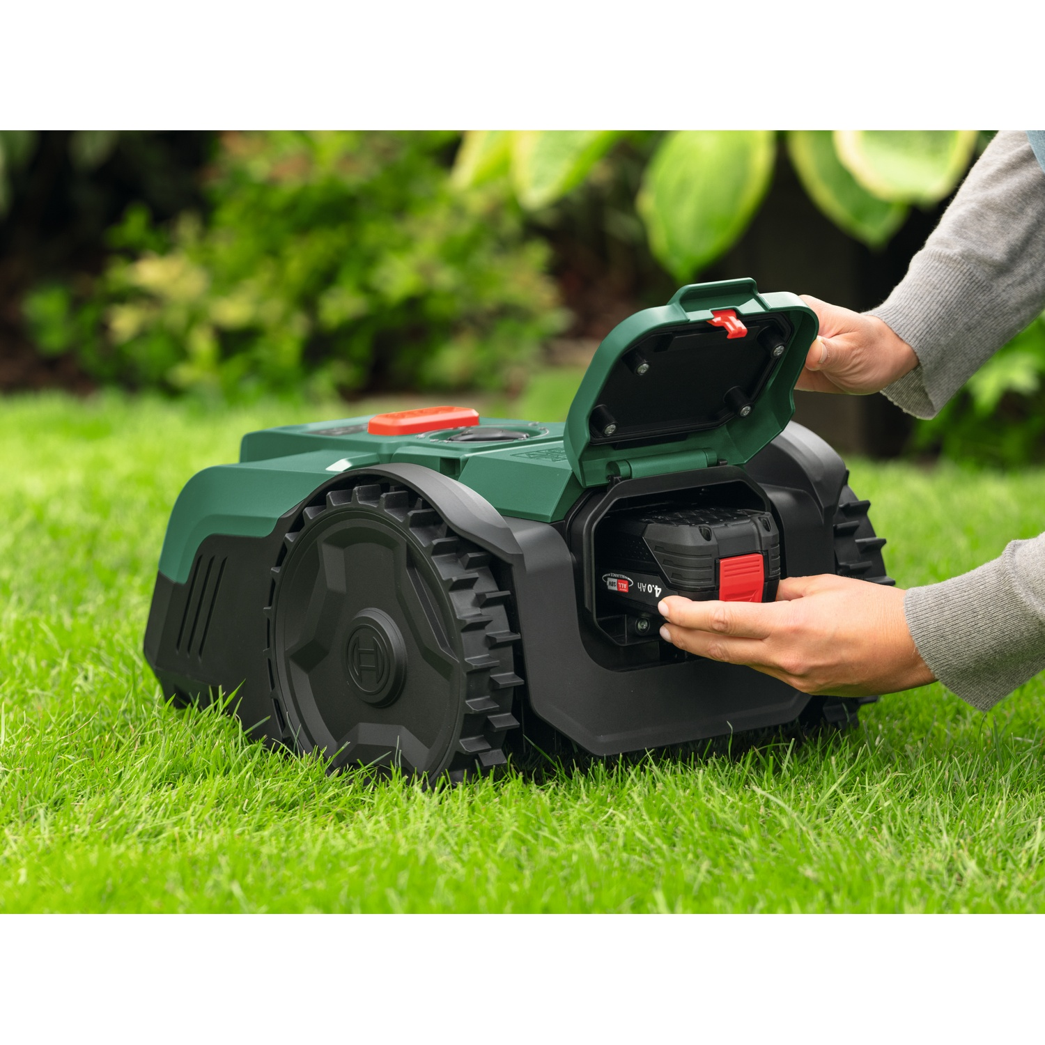 Una mano inserisce una batteria in un robot tosaerba verde sull'erba.