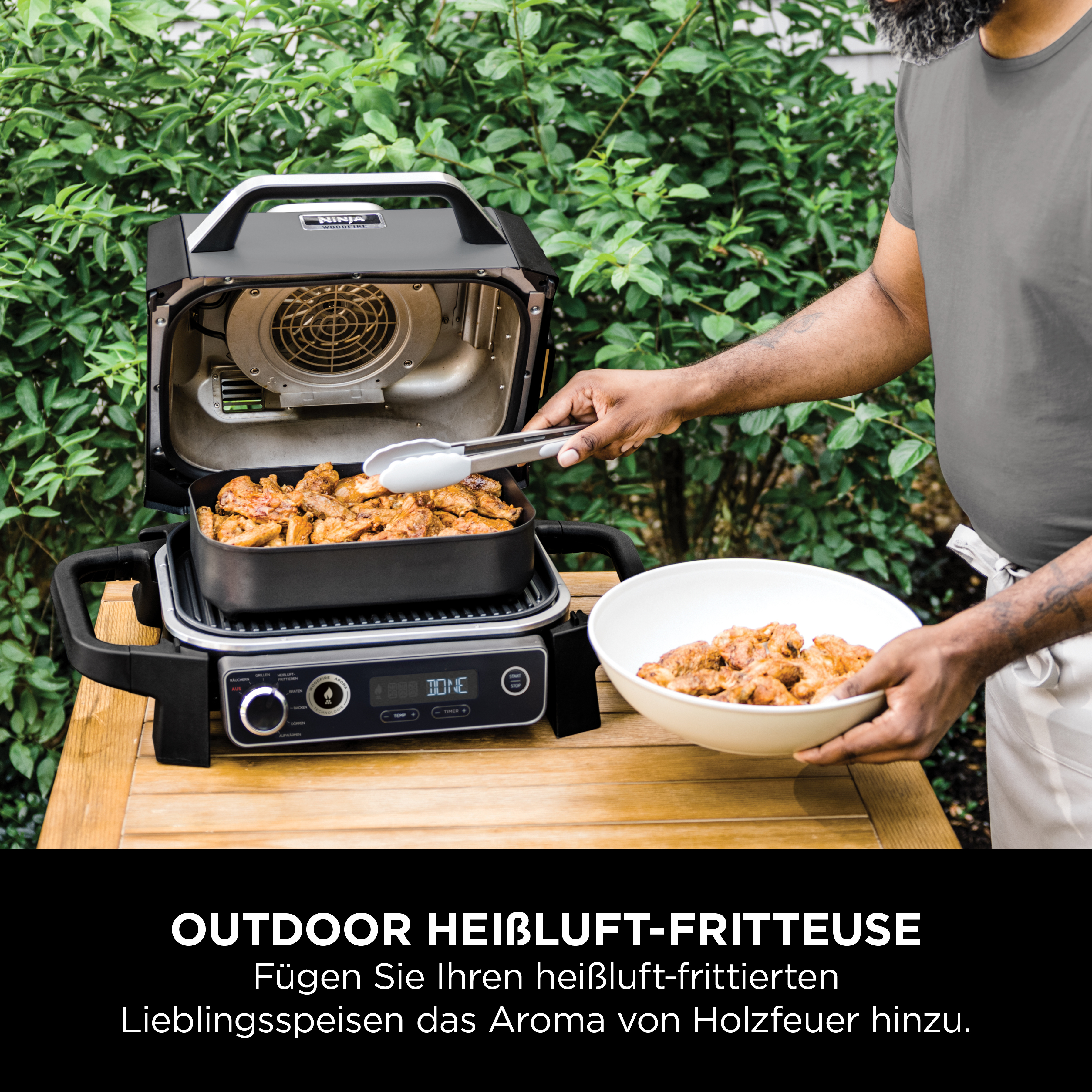 Mann nimmt gegrilltes Hähnchen aus einer Heißluftfritteuse im Freien.