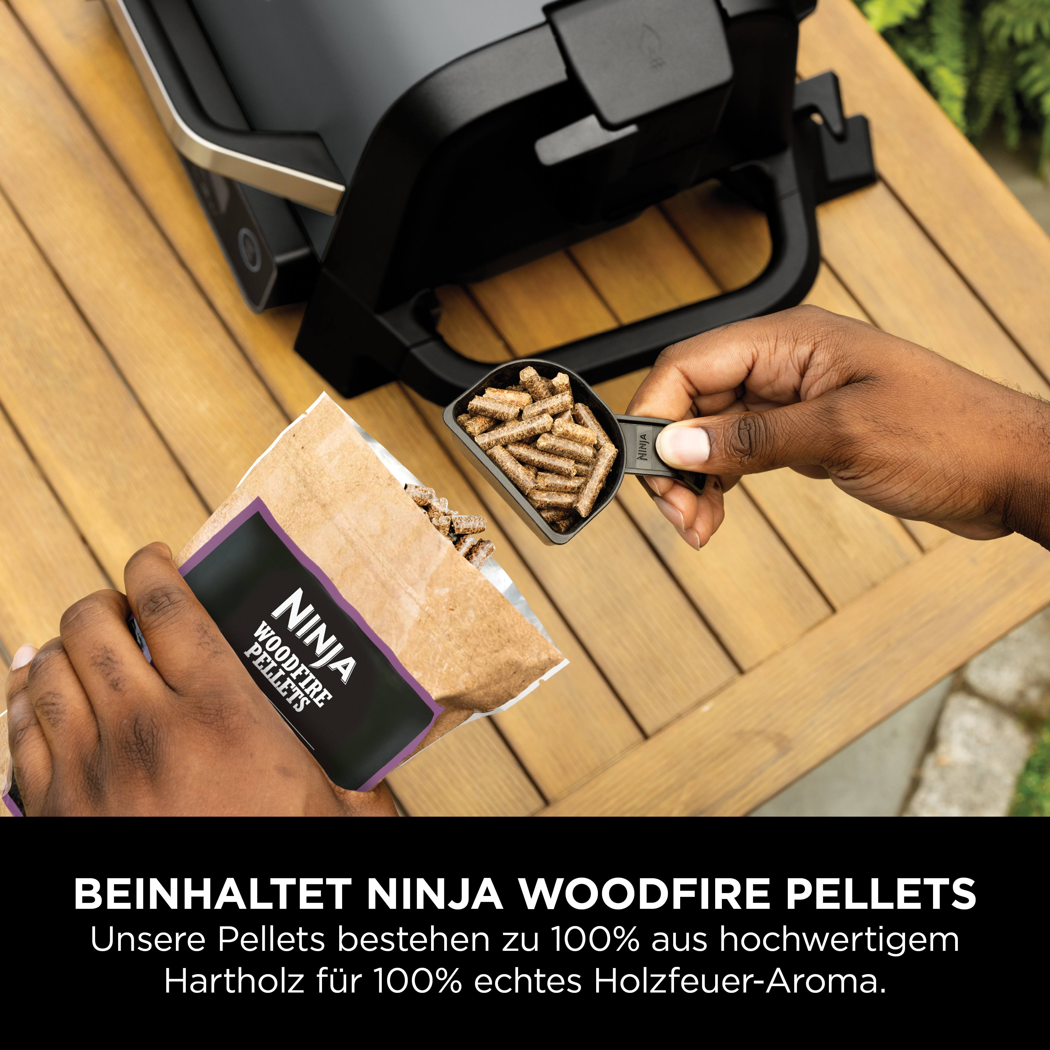 Hände schöpfen Holzpellets aus einer Papiertüte in einen schwarzen Löffel.