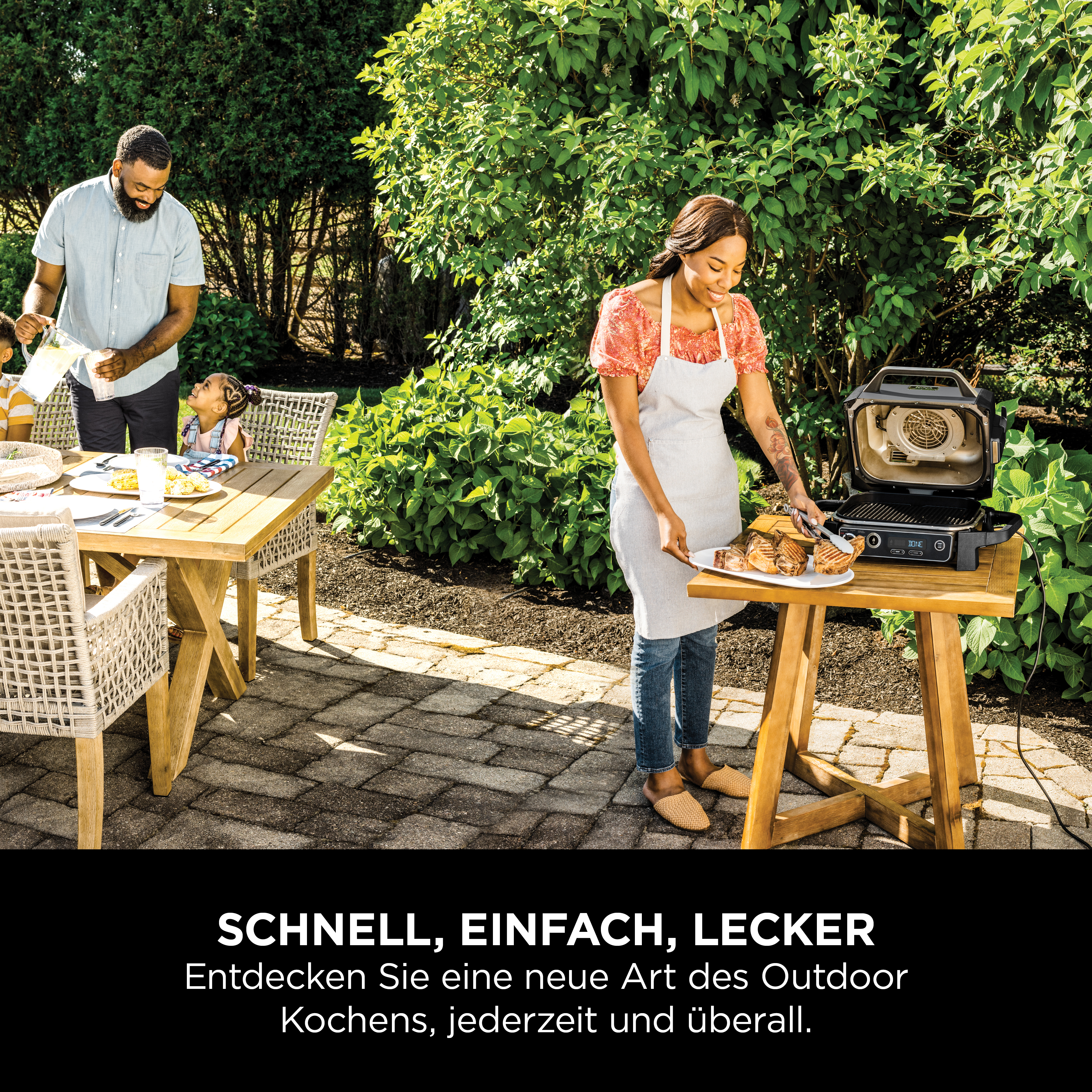 Familie genießt ein Picknick im Garten mit Grill und Essen auf dem Tisch.