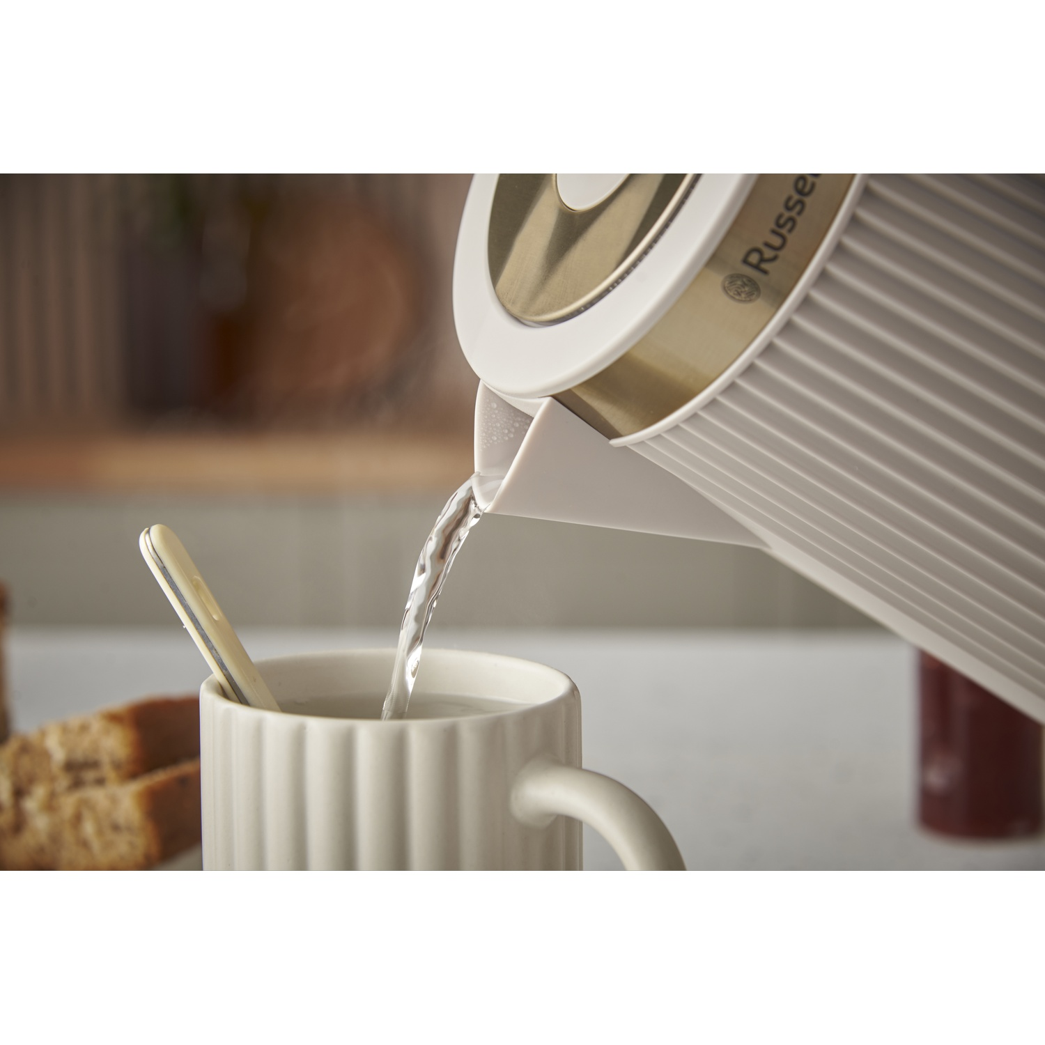 Hot water is being poured from a kettle into a mug. Two slices of bread on the side.