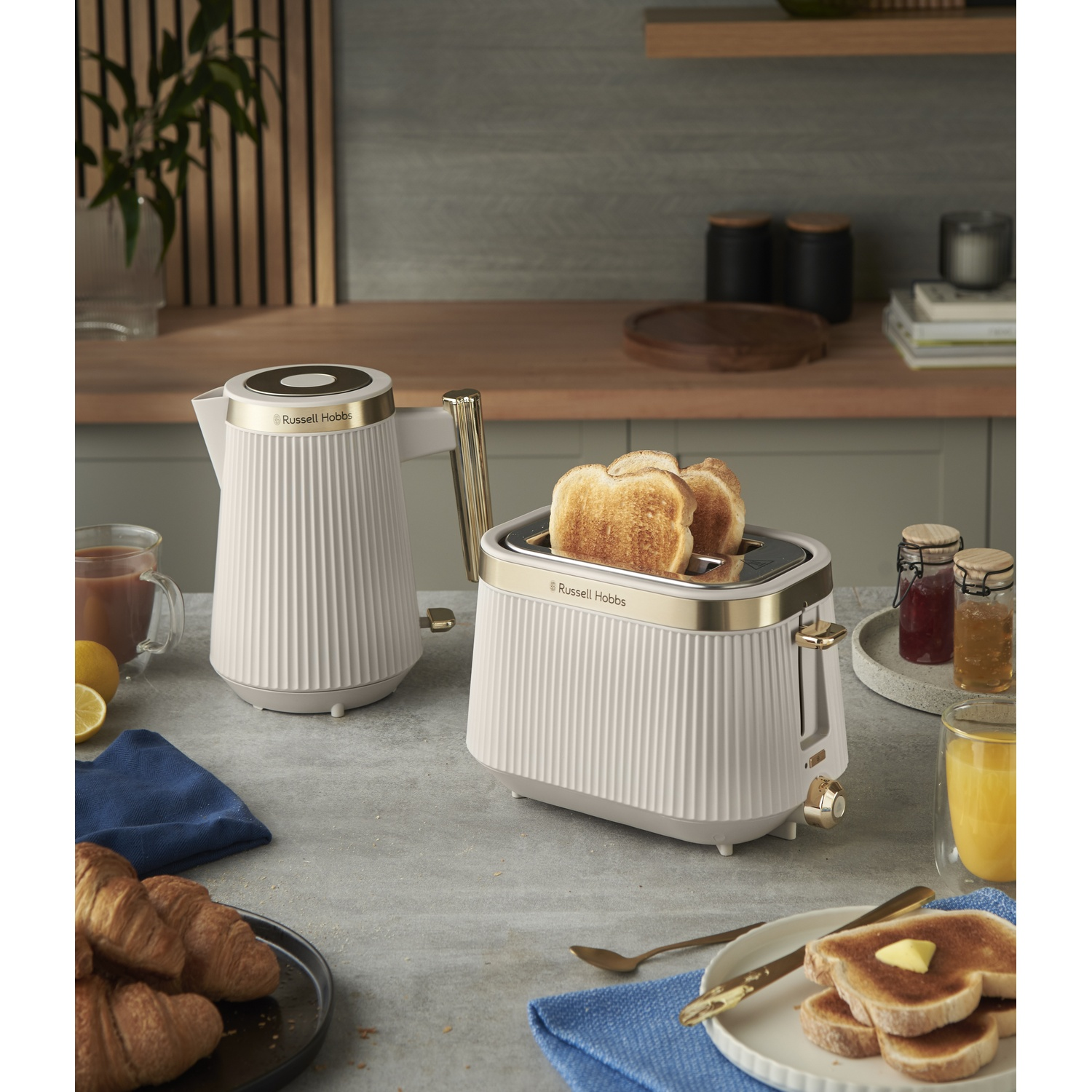 A white kettle and toaster with gold accents on a kitchen counter. Toast pops from toaster.
