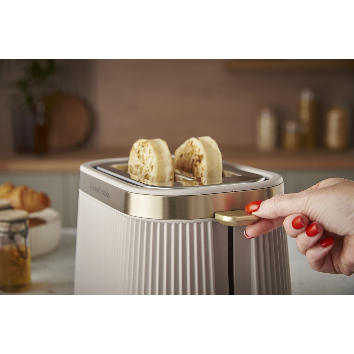 A hand with red nails operates a toaster with two slices of toast.
