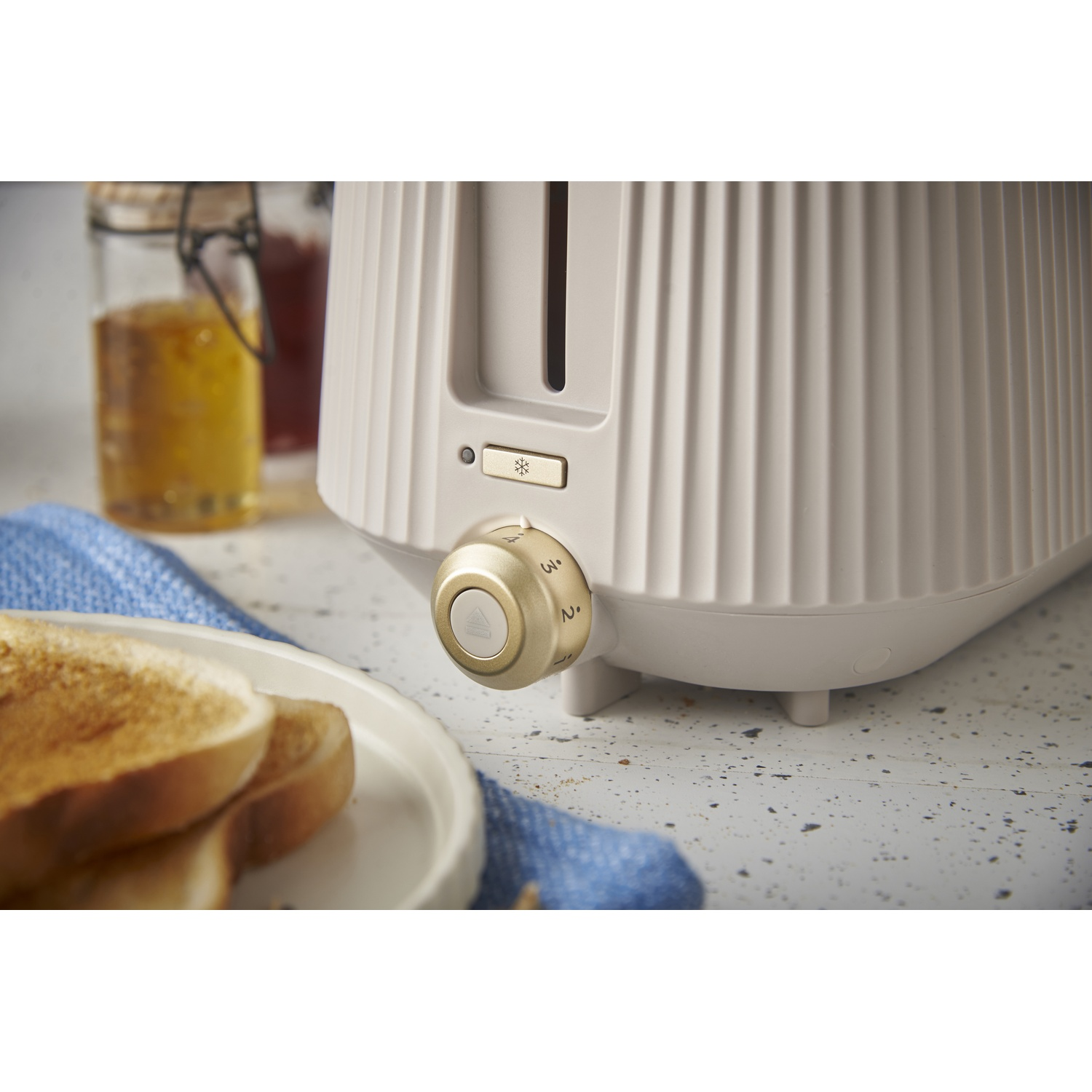 A cream-colored toaster with a gold dial and toast on a plate.