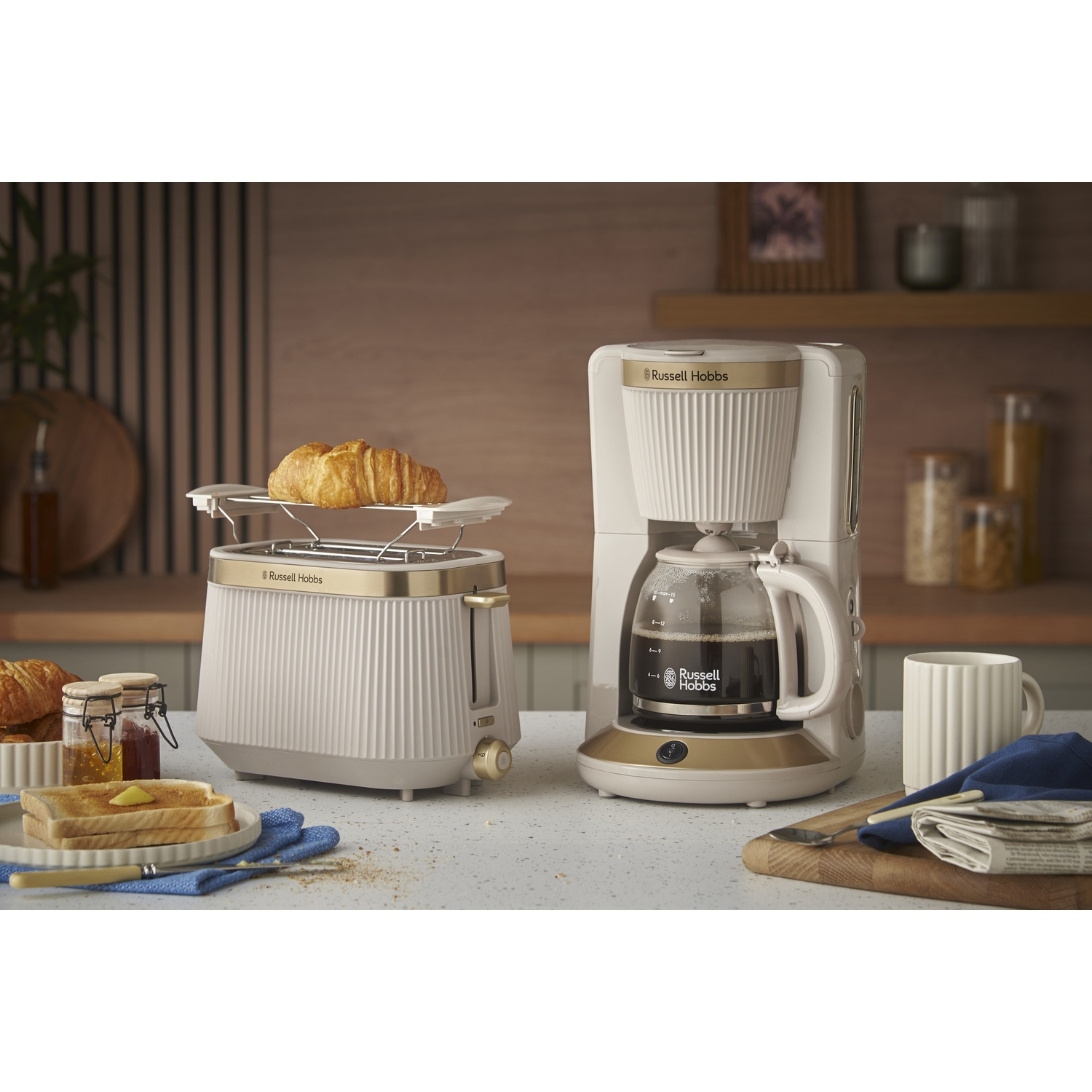 A toaster with a croissant, coffee maker with coffee, and toast with jam.