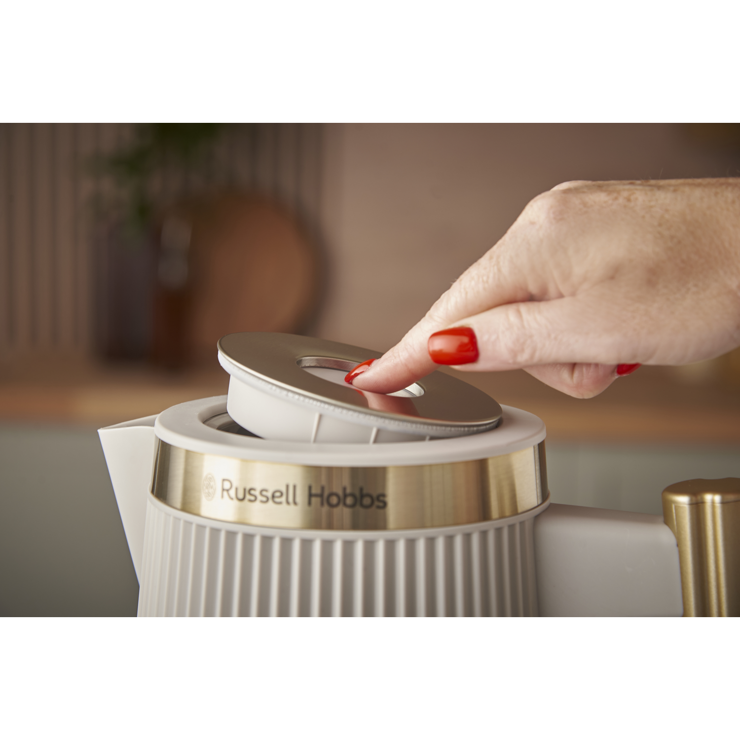 A hand with red nails opens the lid of a white kettle.