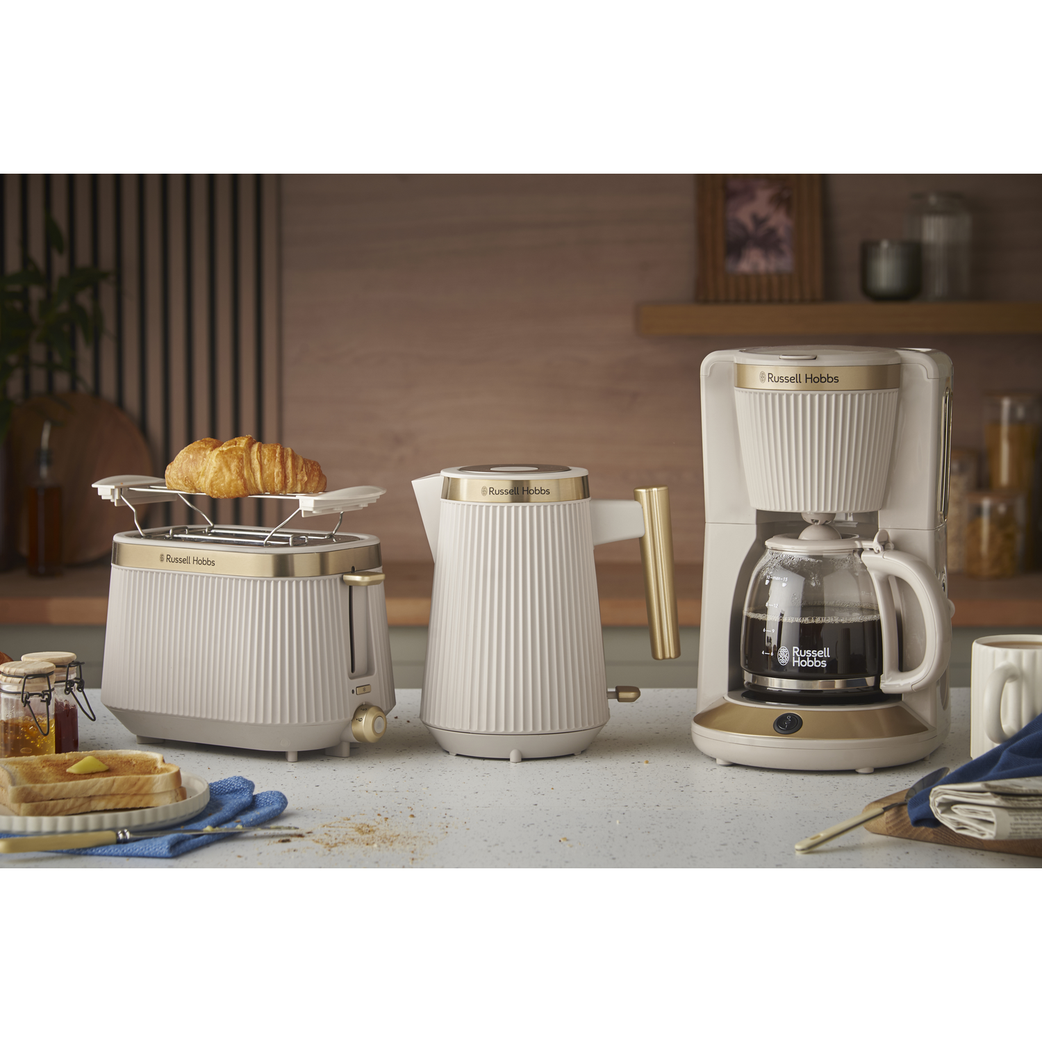 Cream Russell Hobbs toaster, kettle, and coffee maker on counter. Croissant in toaster.