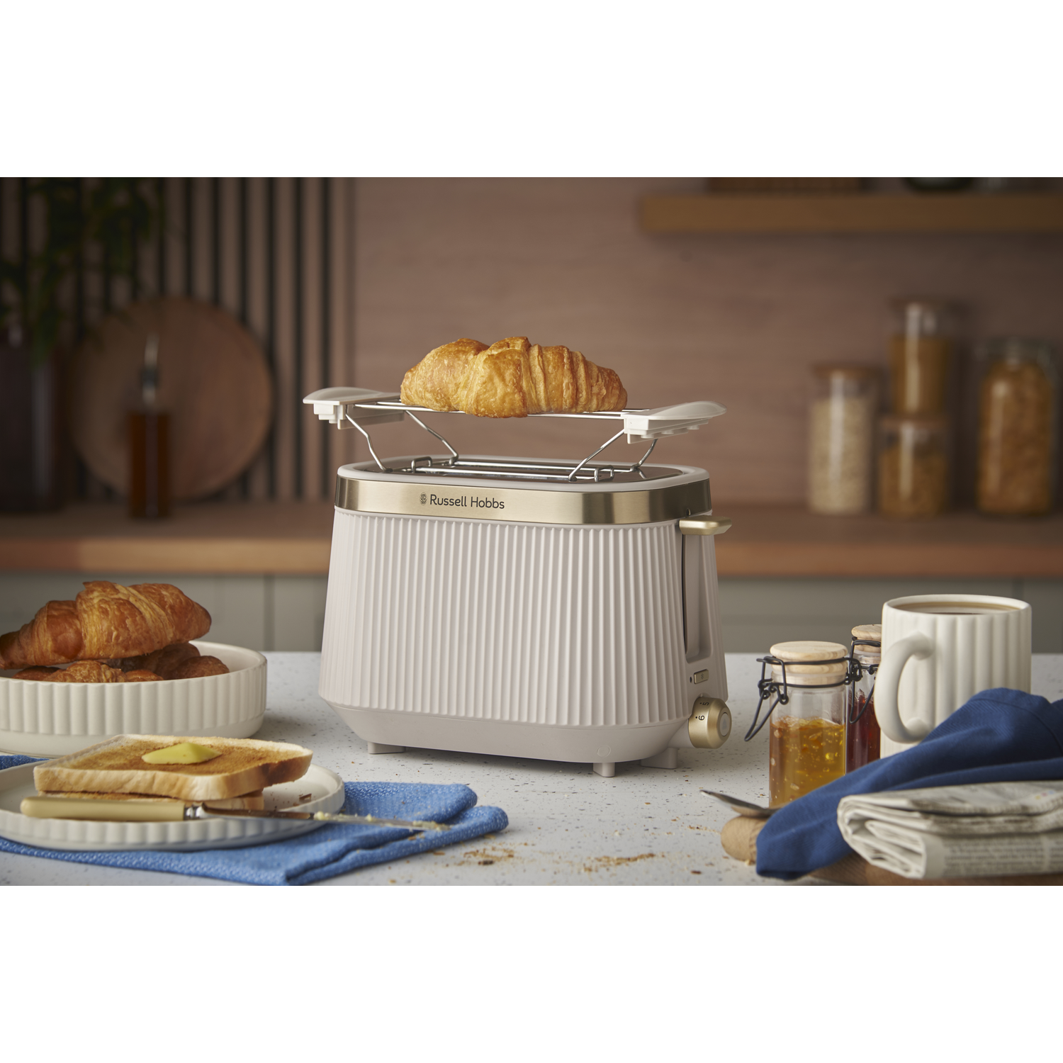 A toaster with a croissant, toast, jam, and coffee.
