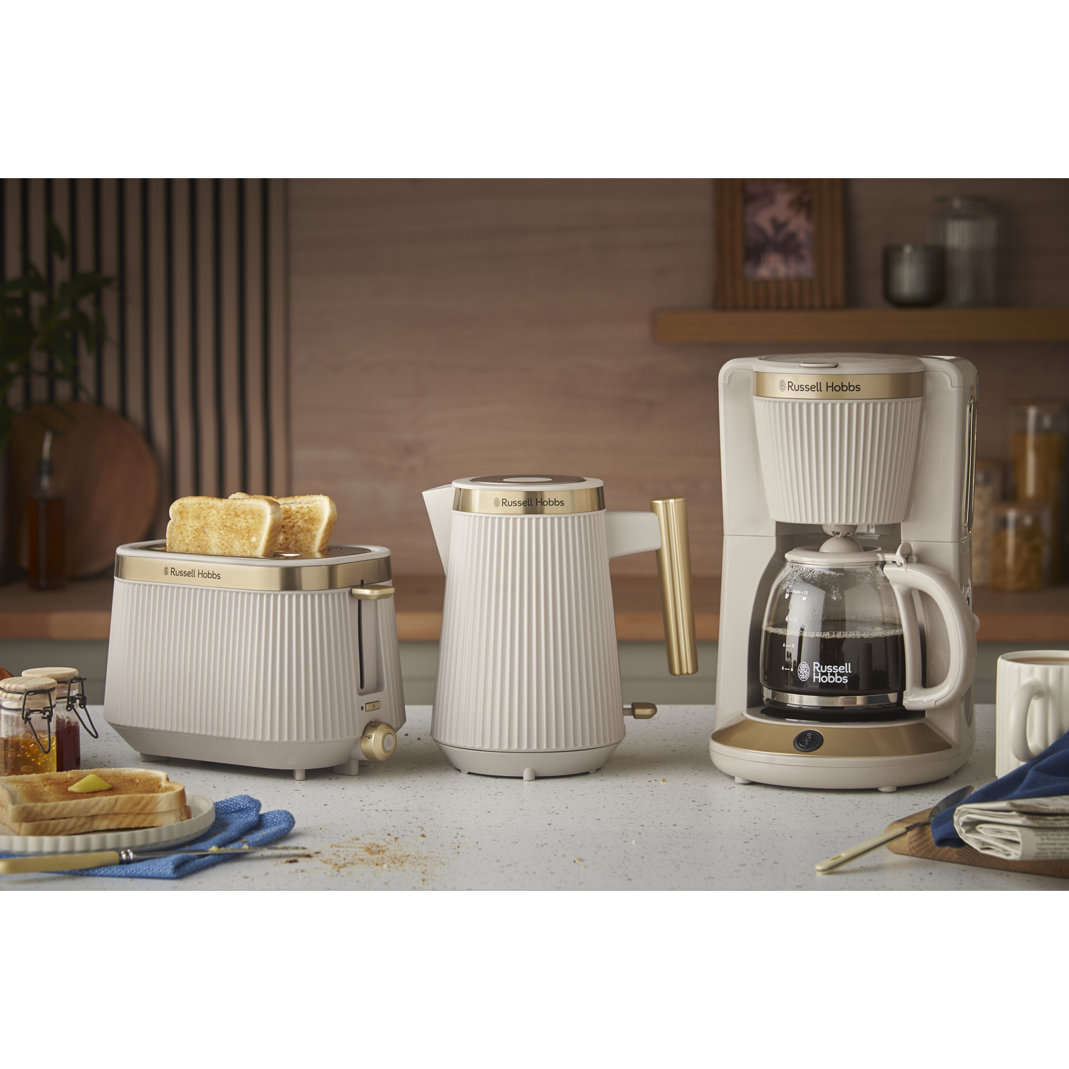 A white toaster, kettle, and coffee maker with gold accents on a countertop.