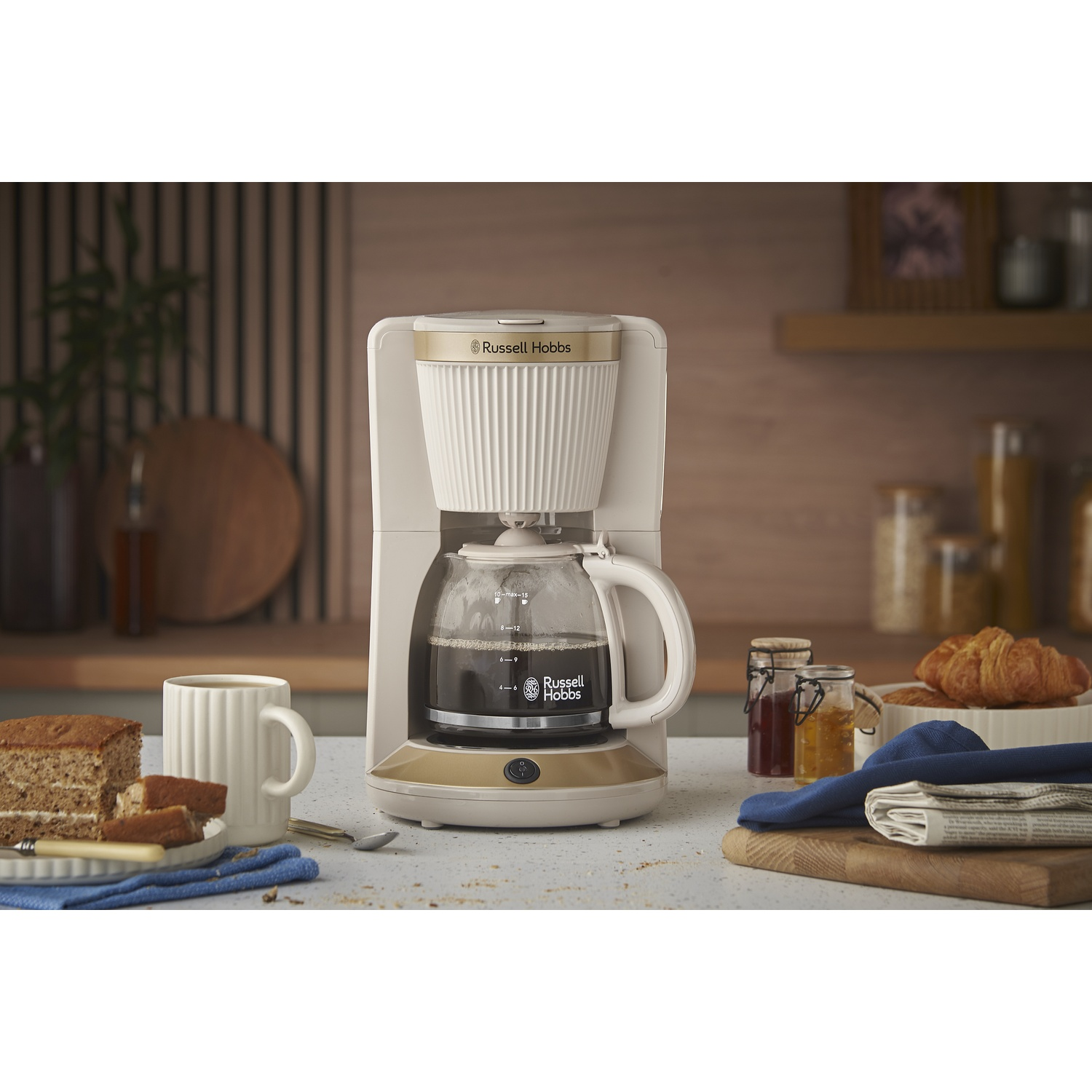 Een koffiezetapparaat zet koffie naast een mok, cake, croissants en potten jam.