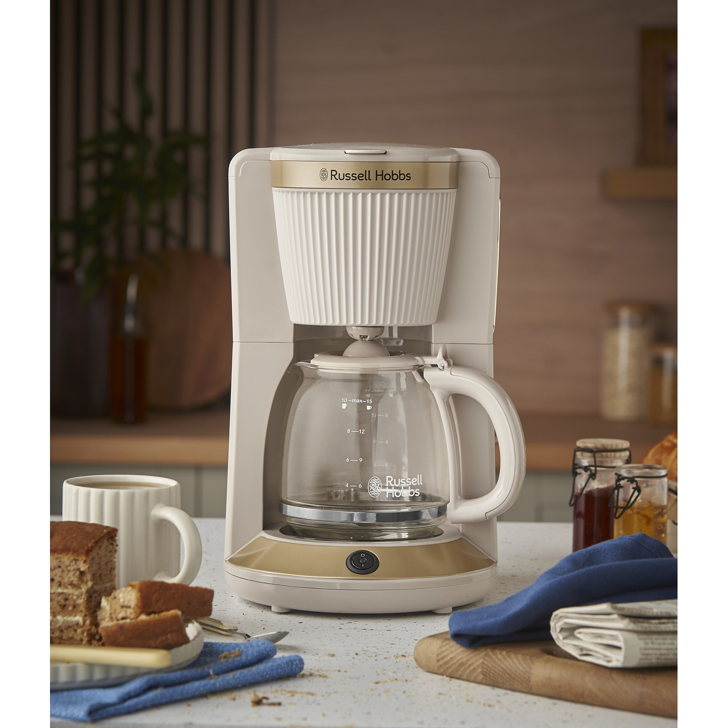 Een Russell Hobbs koffiezetapparaat met glazen kan op een aanrecht met cake en koffie.