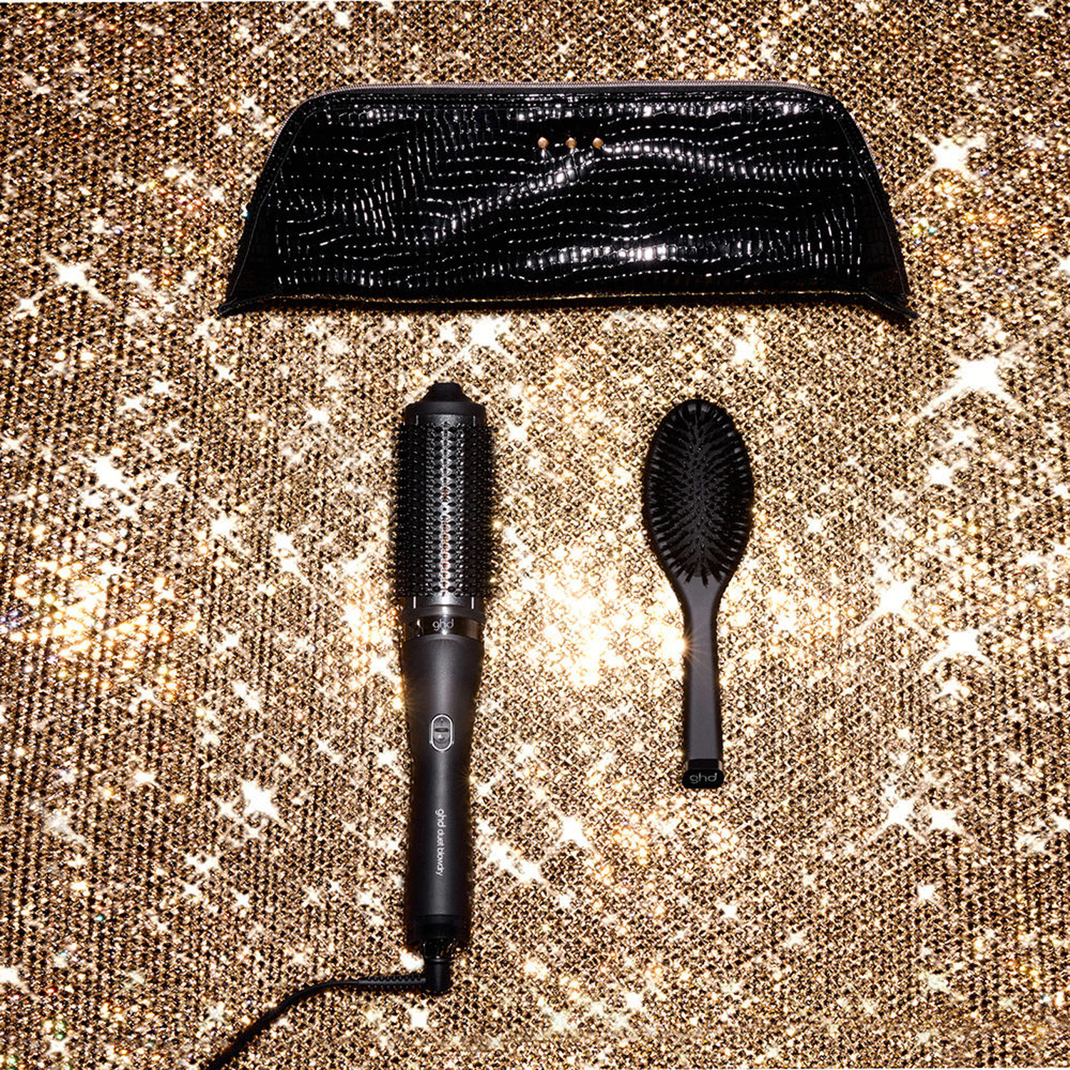 Black hair brush, styler and bag on a sparkly gold background.
