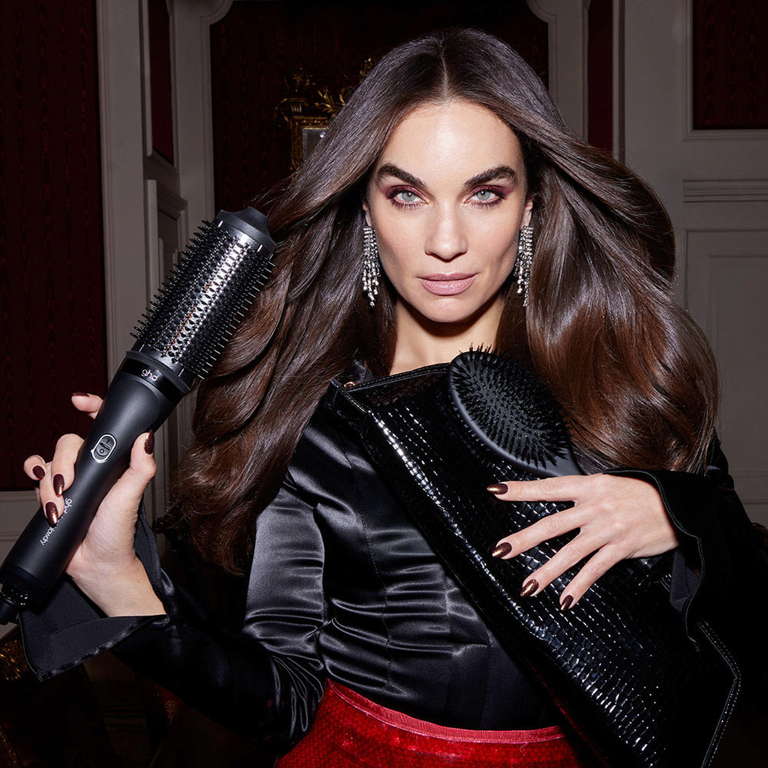 Woman with long hair holds a black curling iron and a brush.