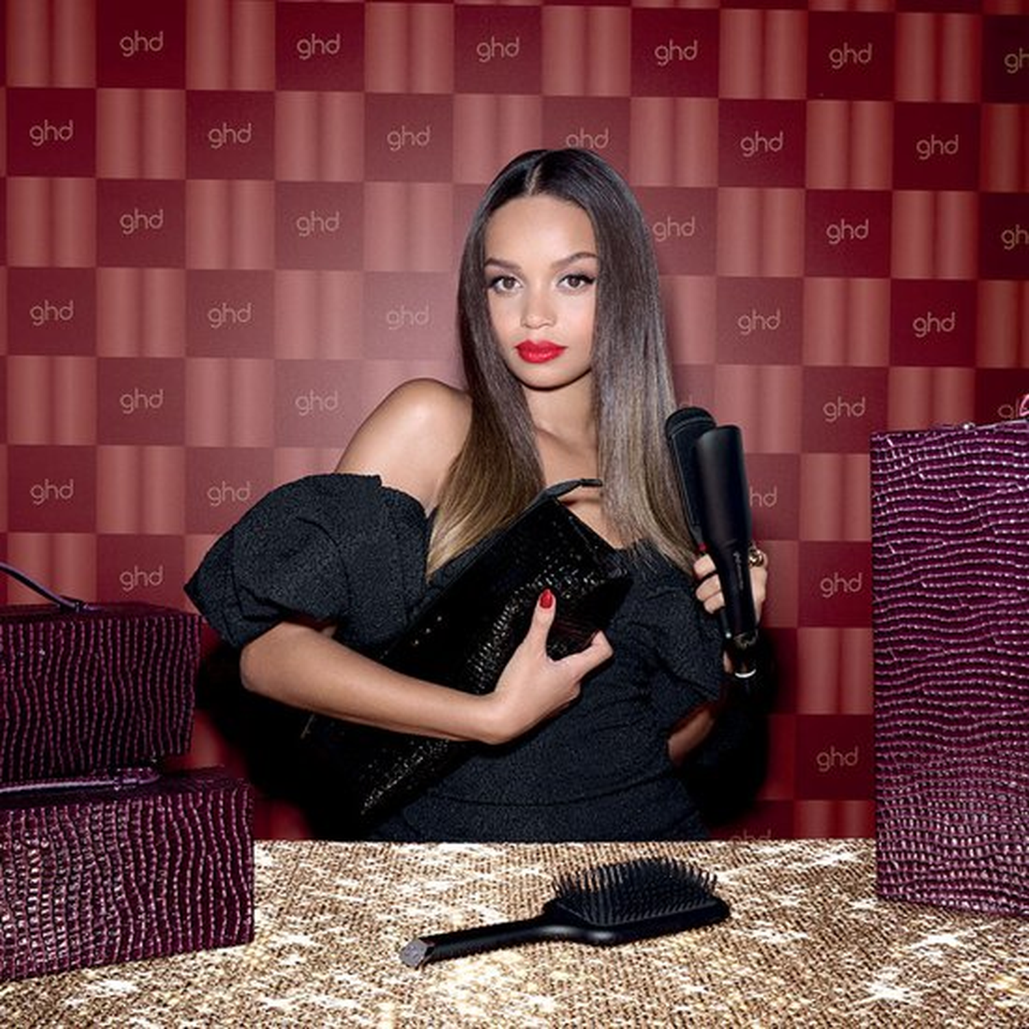 A woman with long hair holds a black hair straightener and a clutch. A brush is in the foreground.