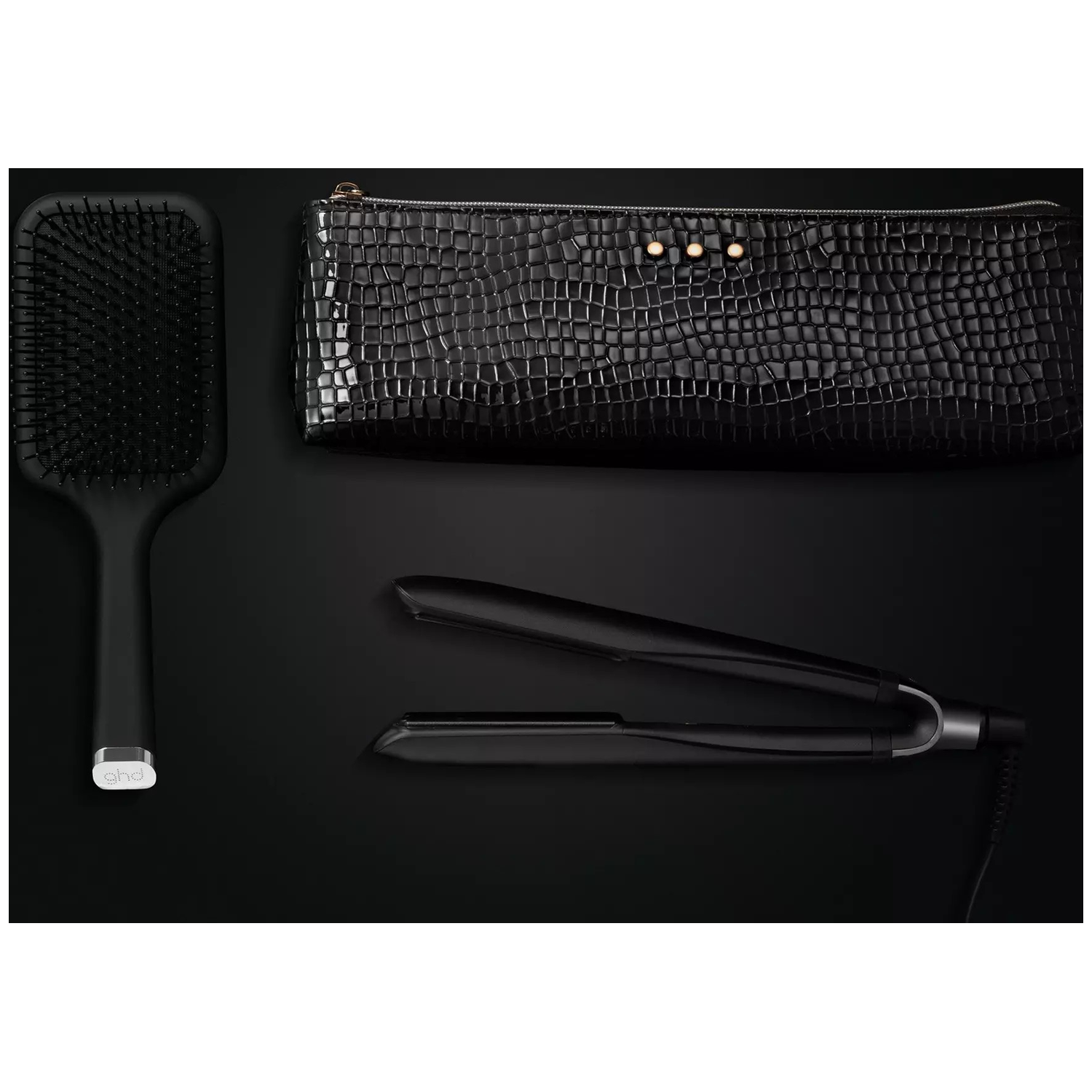 A black hair straightener, brush and cosmetic bag on a black background.