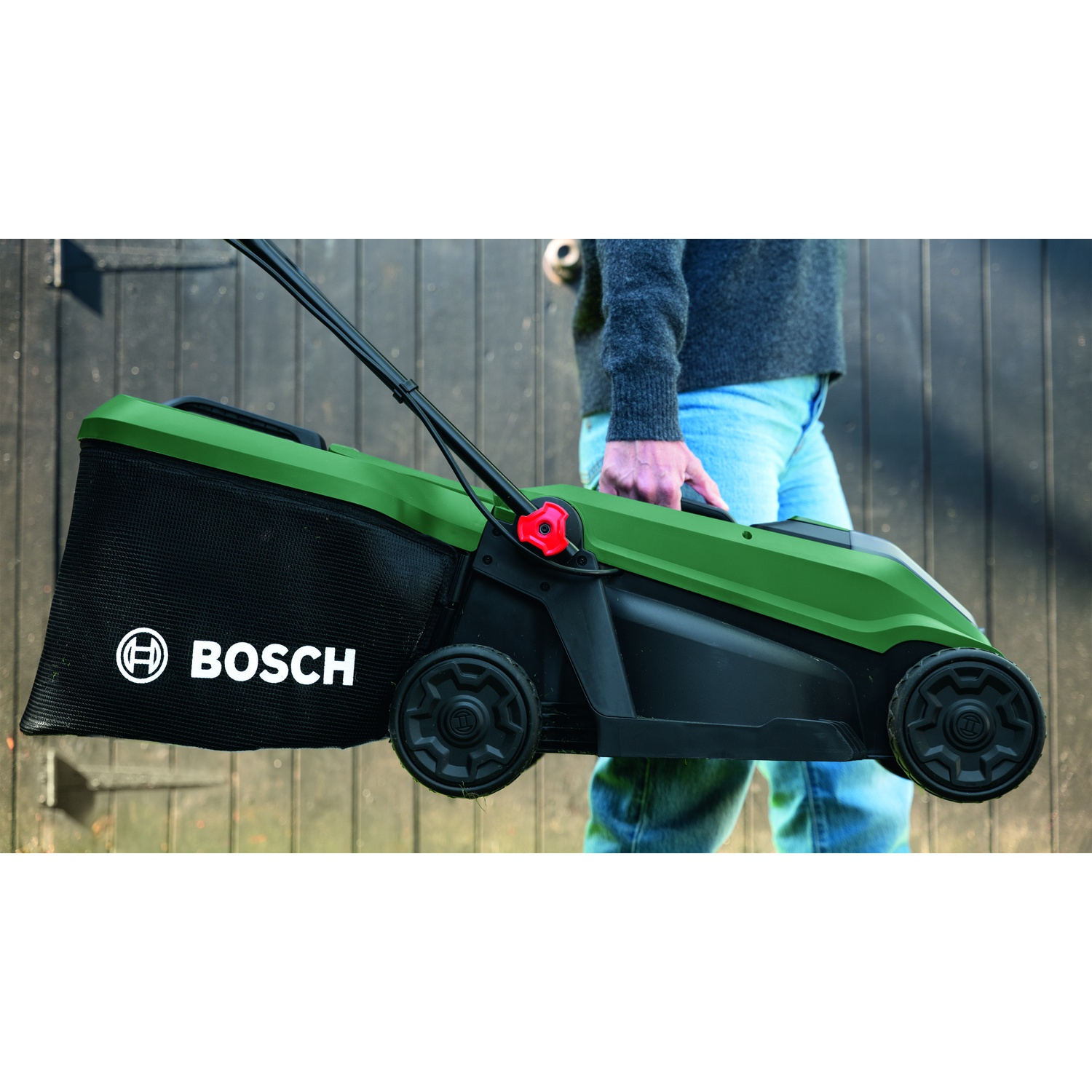 Tosaerba verde Bosch con cesto, tenuta da persona in jeans.