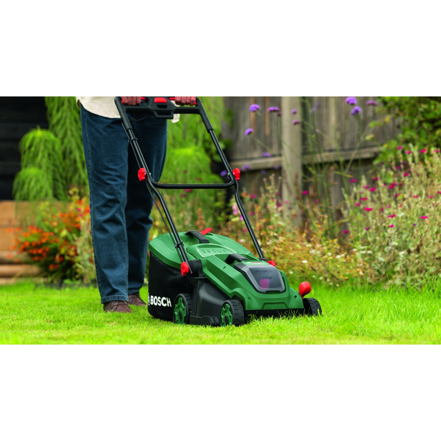 Una persona taglia un prato verde con un tosaerba Bosch verde in un giardino.
