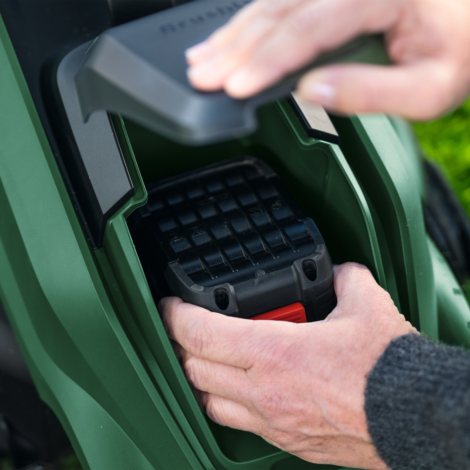 Mani inseriscono una batteria in un tosaerba verde.