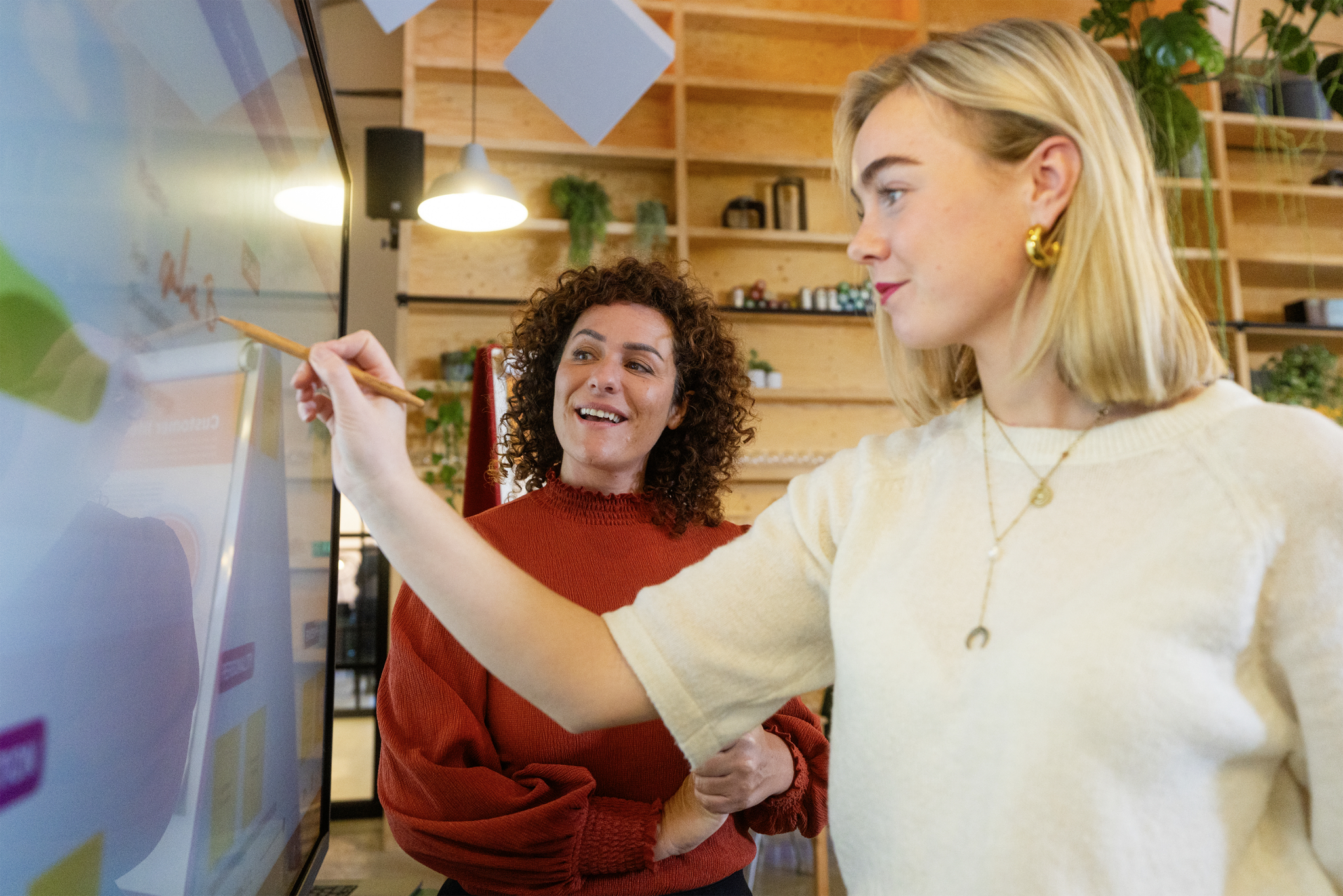 Zwei Frauen interagieren mit einem Touchscreen in einem Büro mit Holzregalen.