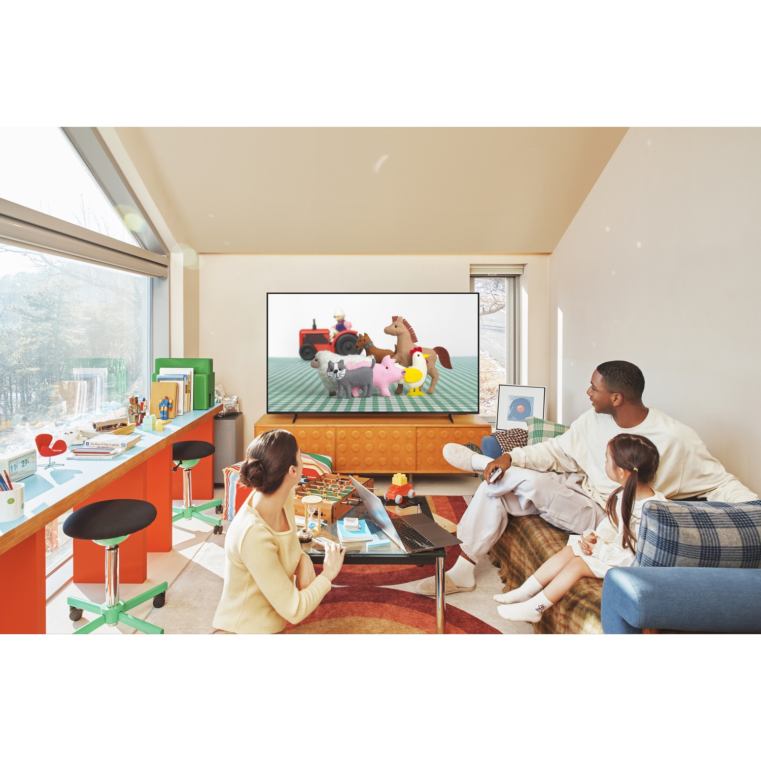 Family watches TV; man, woman, and child on sofa. Woman works on laptop.