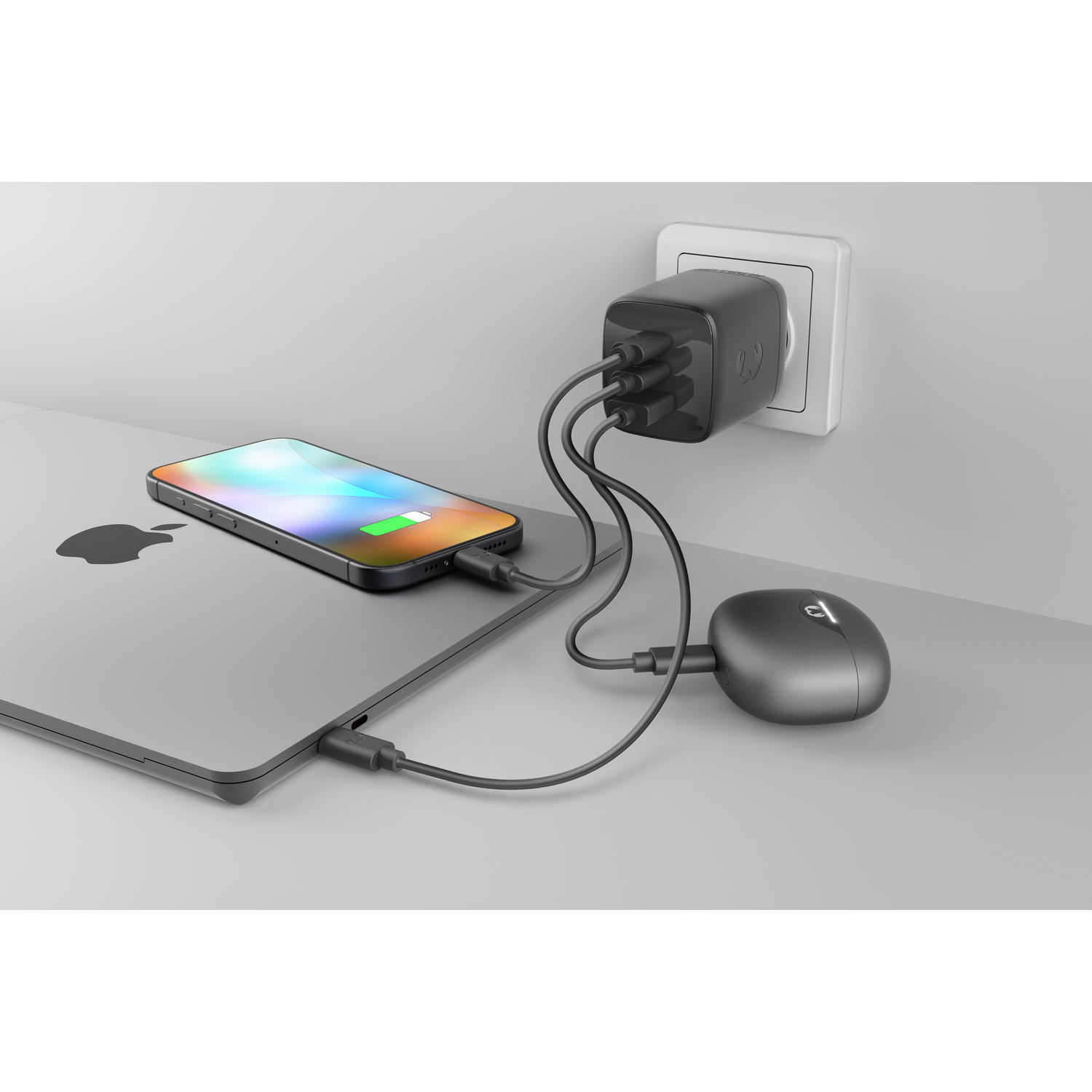 A black power adapter charges a phone and earbuds on a laptop.