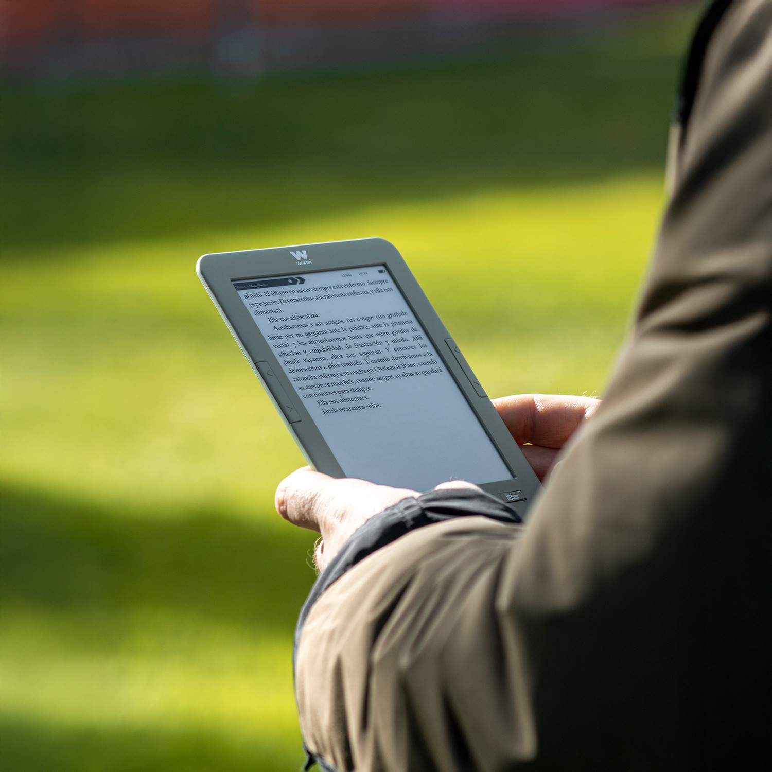 Una persona sostiene un lector electrónico al aire libre. La pantalla muestra texto.