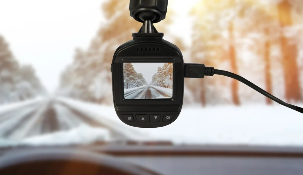Kamera samochodowa nagrywa zaśnieżoną drogę z drzewami w tle.